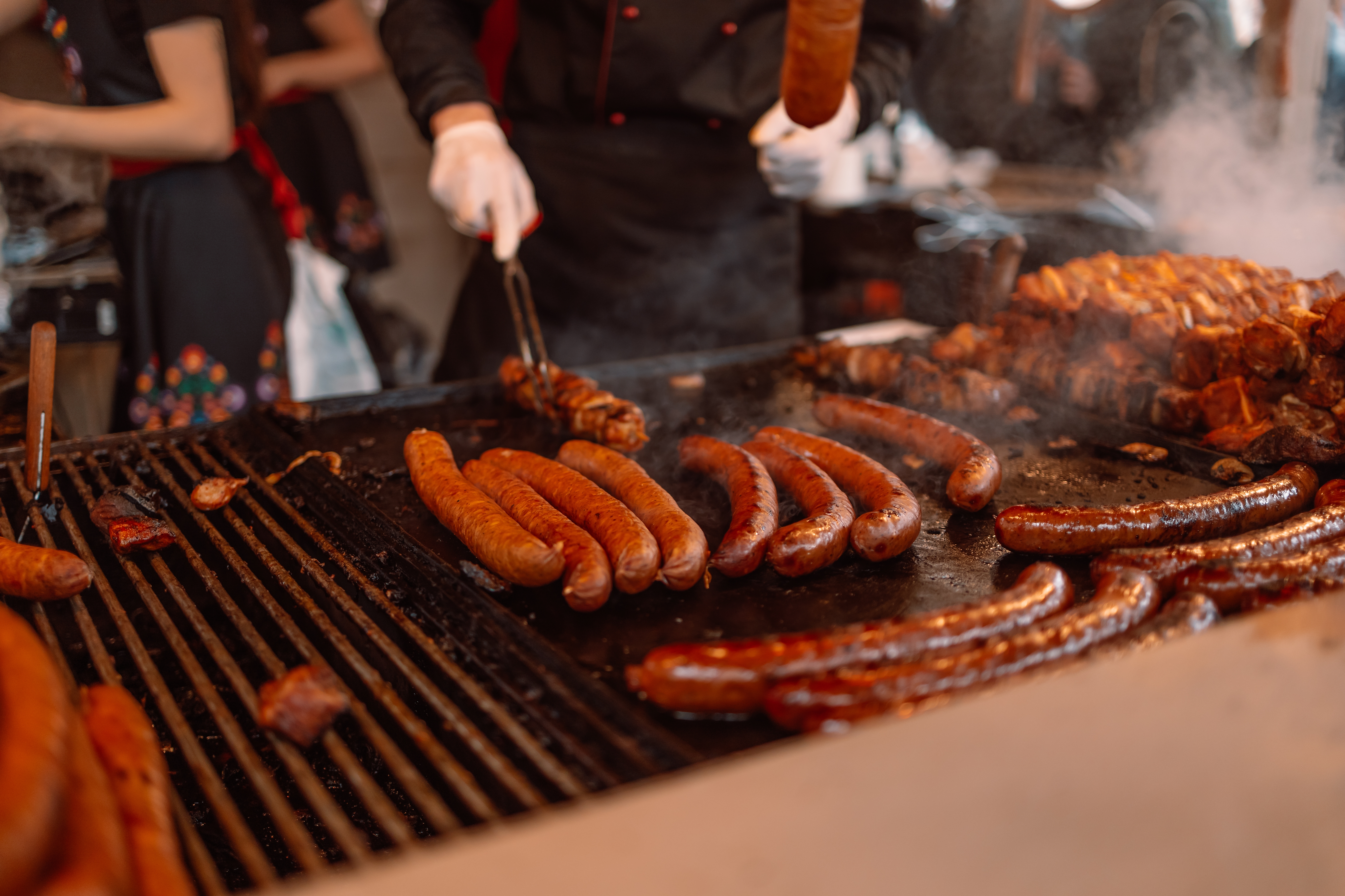Saftige grillede pølser på et travlt street food marked i Krakow, Polen, tilberedt af en kok i sort tøj med hvide handsker