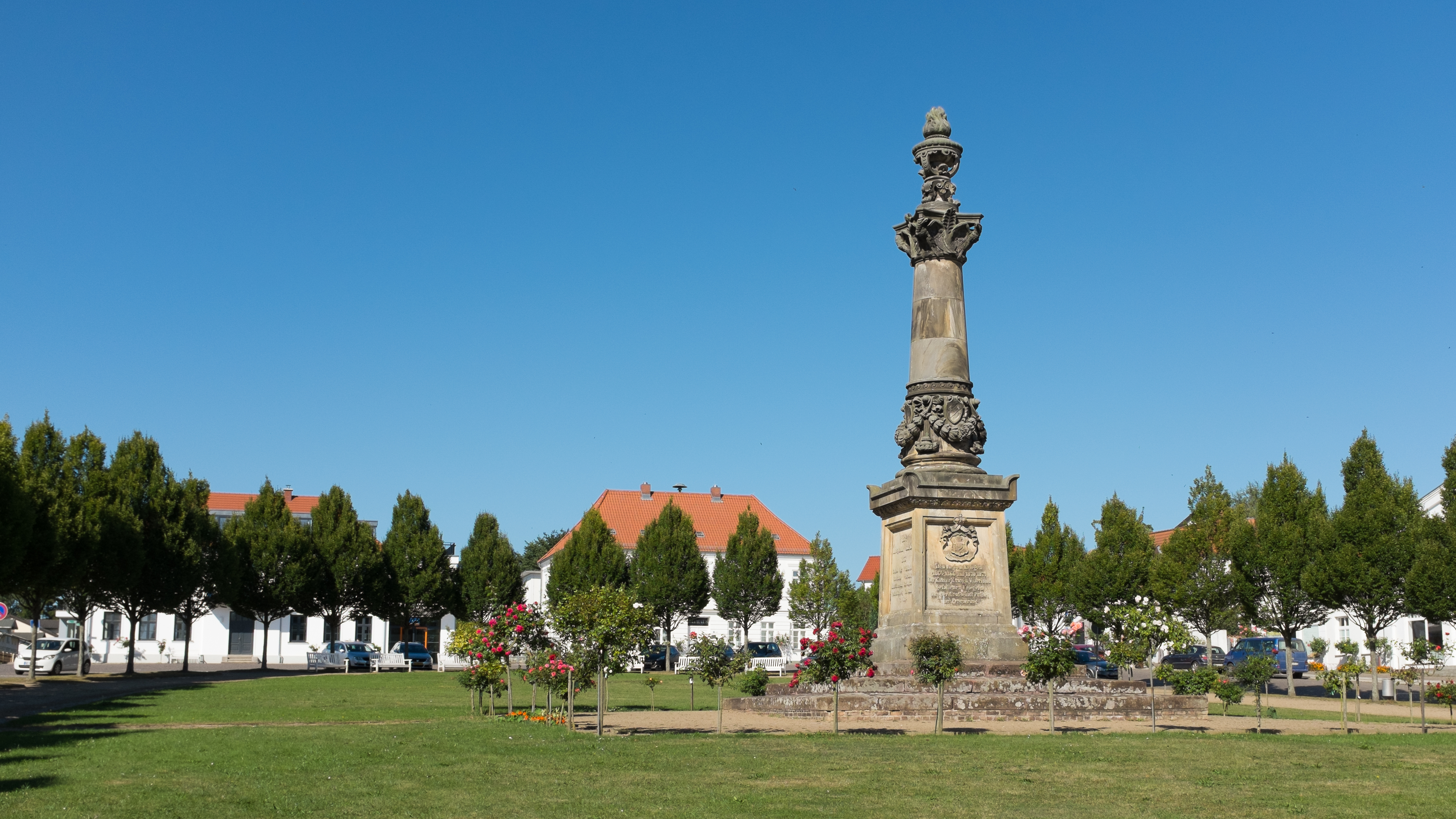 Stately krigsmonument omgivet af grønne træer og hvide huse