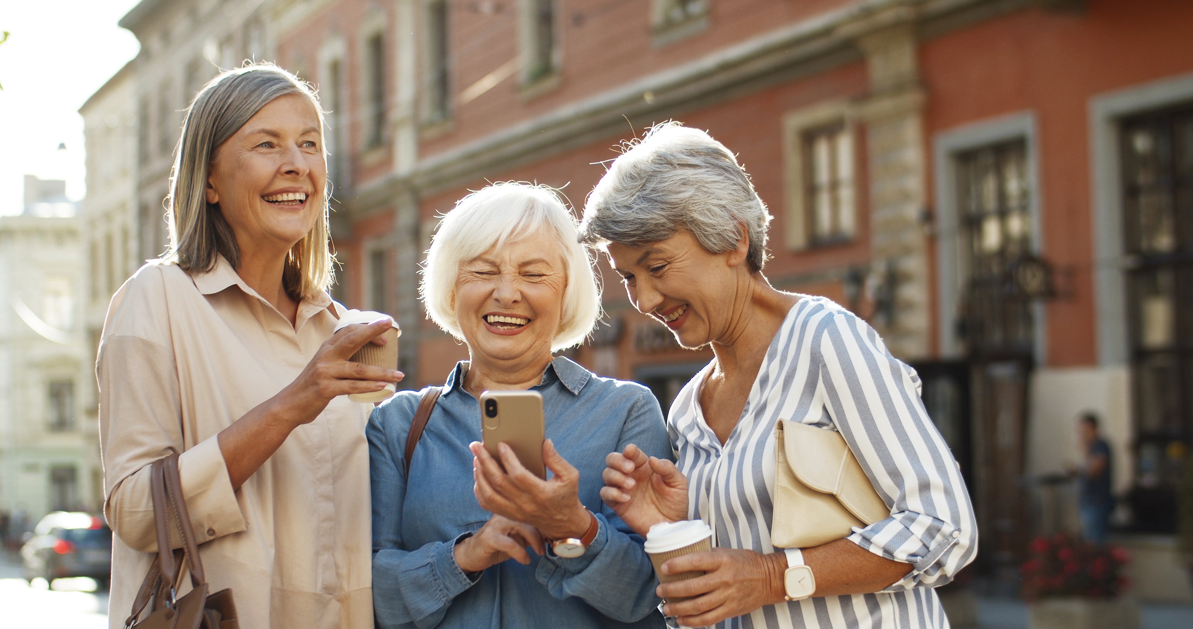 Gruppe af kvinder griner af noget på mobilen foran smukke historiske bygninger