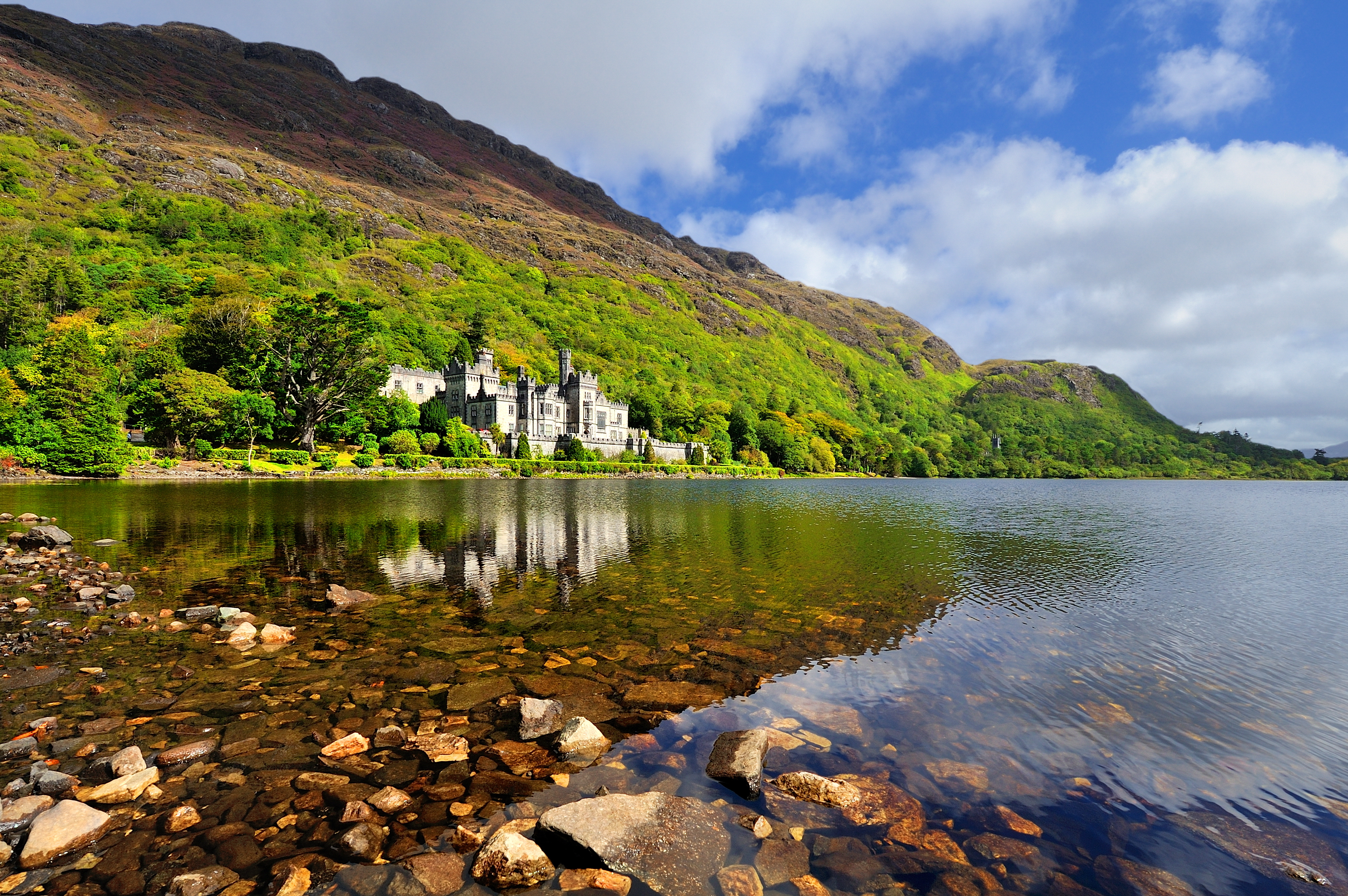 Det smukke Kylemore Abbey ved søen i Connemara, Irland, med grønne bjerge og fredfuldt vand i forgrunden