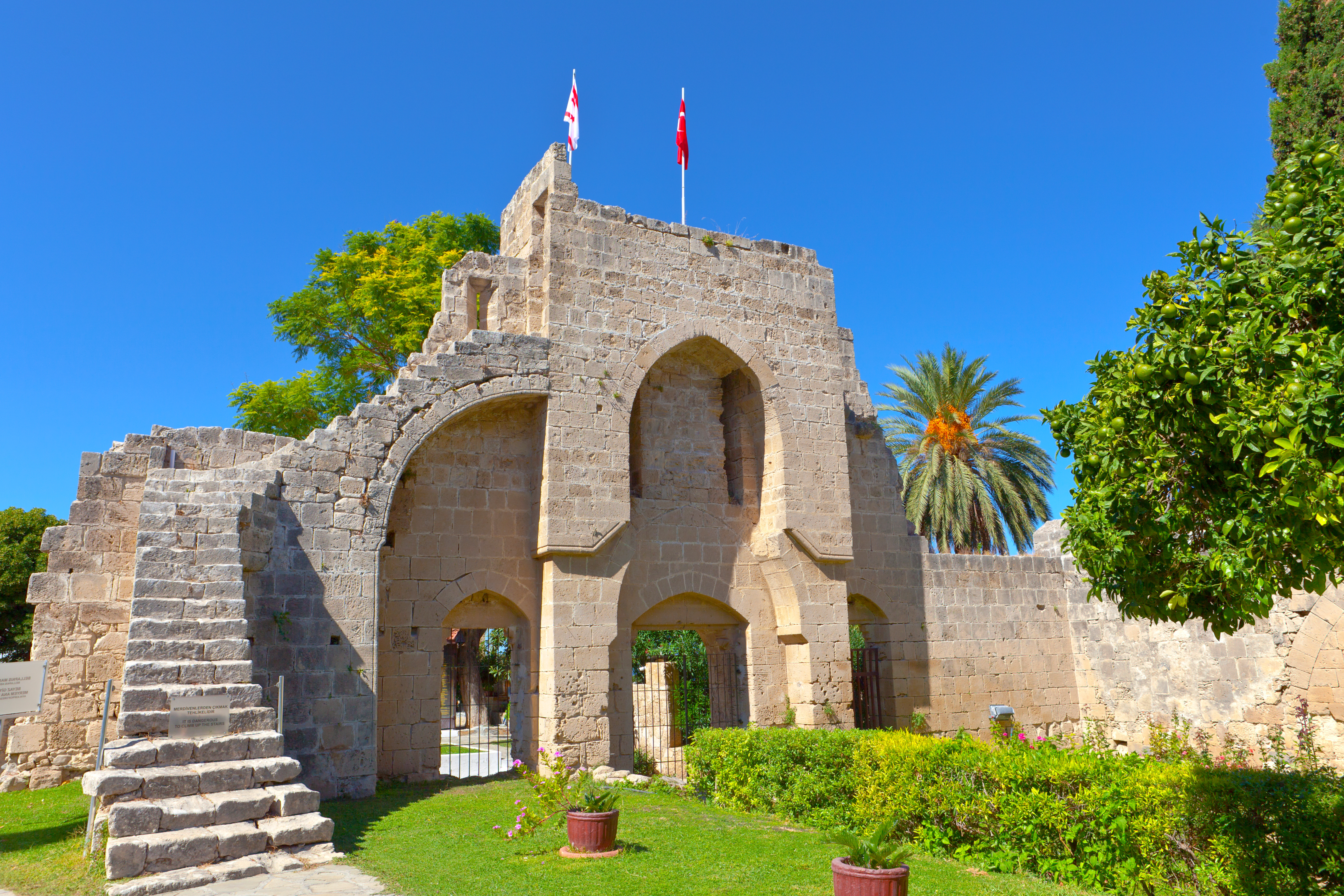 Smukke ruiner af det historiske Bellapais Abbey ved Kyrenia på Nordcypern med gotiske stenbuer og palmer