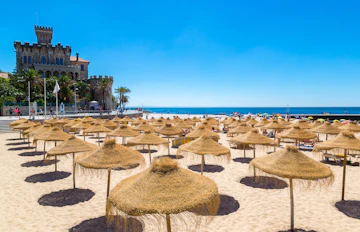 Fantastisk kystområde med sandstrand, halmparasoller og historisk borg ved det krystalklare hav