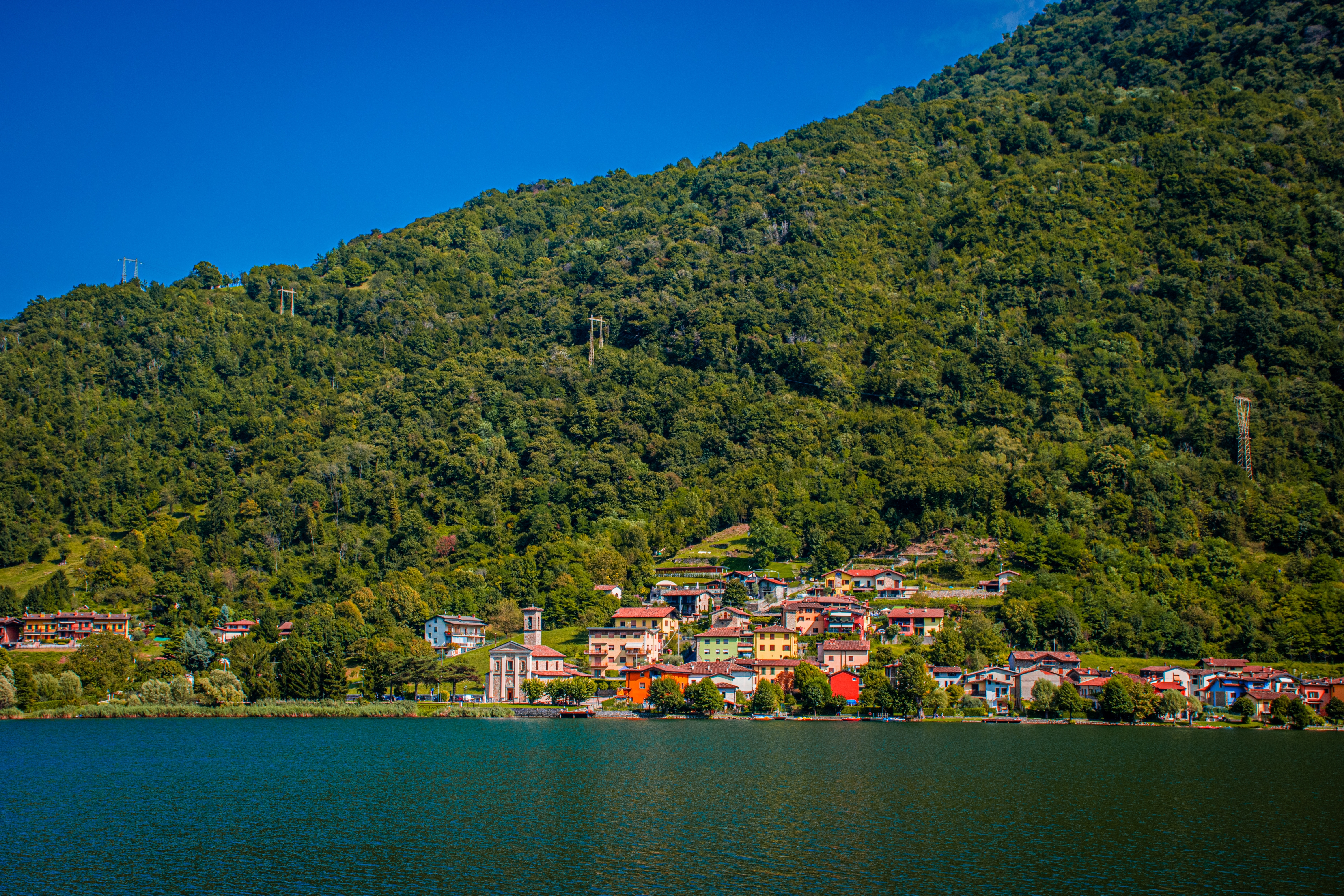Malerisk udsigt over Lake Iseo med en lille italiensk landsby ved vandkanten omgivet af grønne bjerge i Lombardiet
