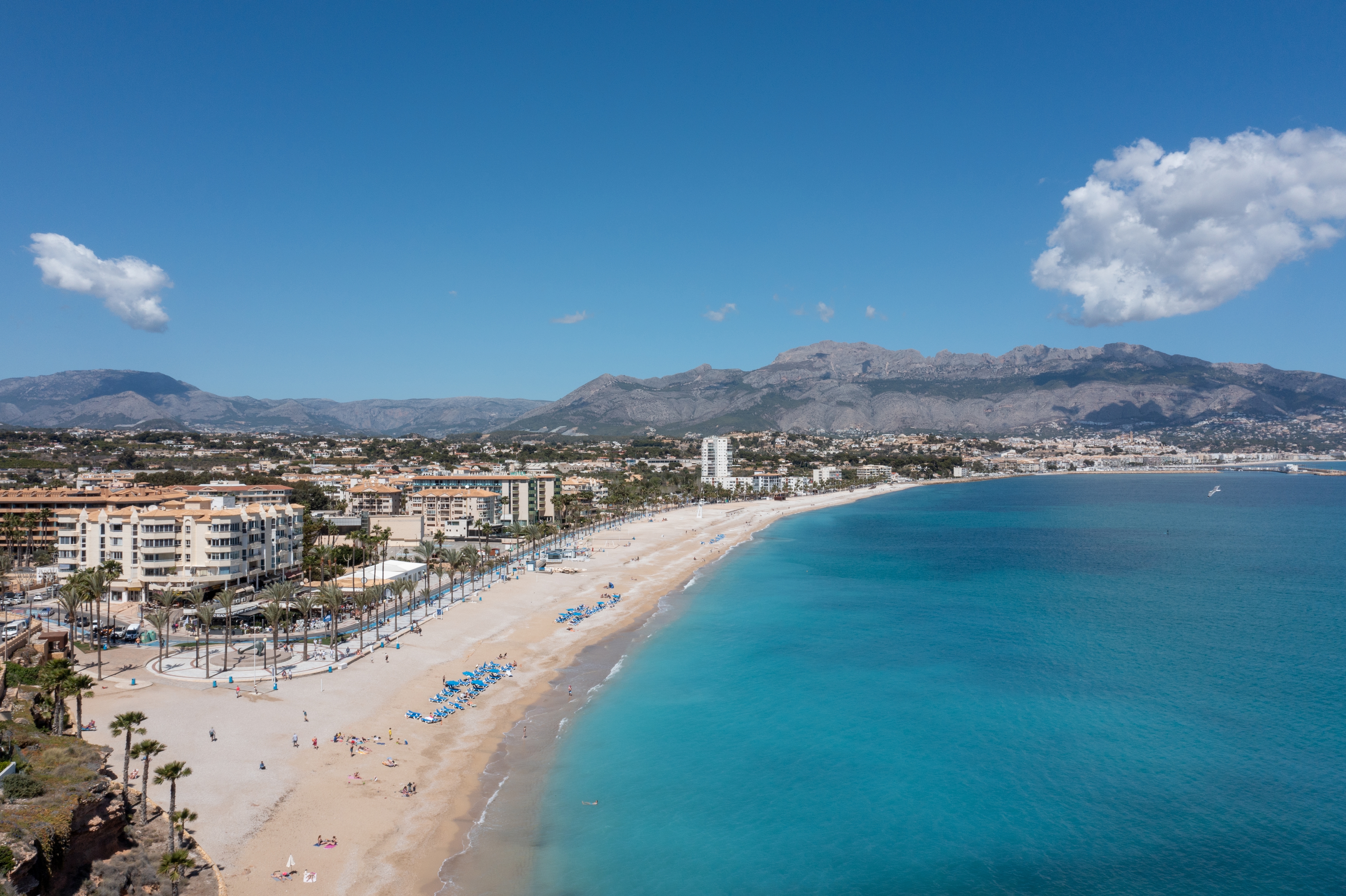 Luftfoto af L'Albir ved Costa Blanca i Spanien med turkisblåt Middelhav, guldgul sandstrand, palmer og bjerge i baggrunden på en solskinsdag