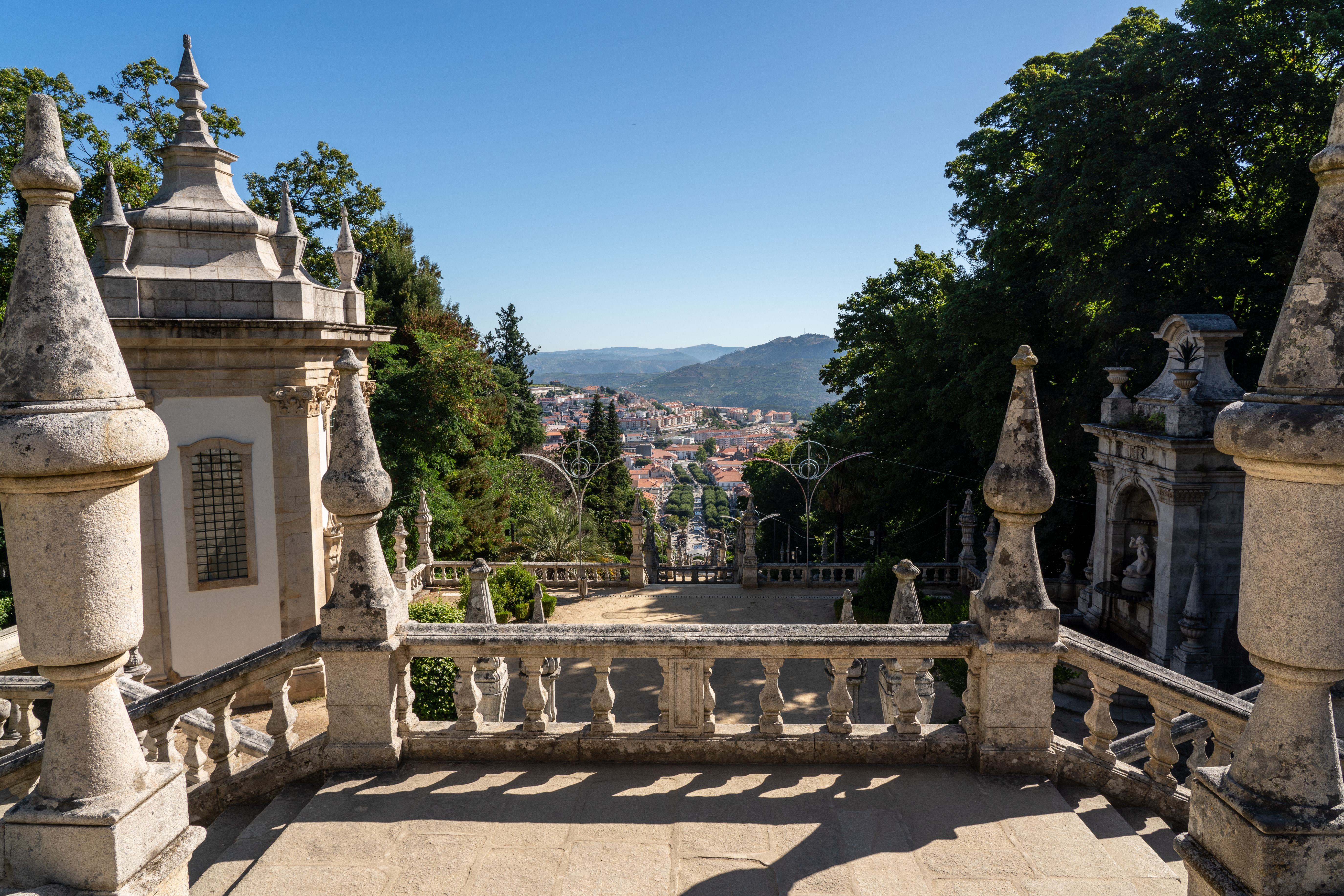 Panoramaudsigt fra Remédios helligdommens barokke trappe i Lamego, Portugal, med ornamenterede stenstatuer og byens røde tage