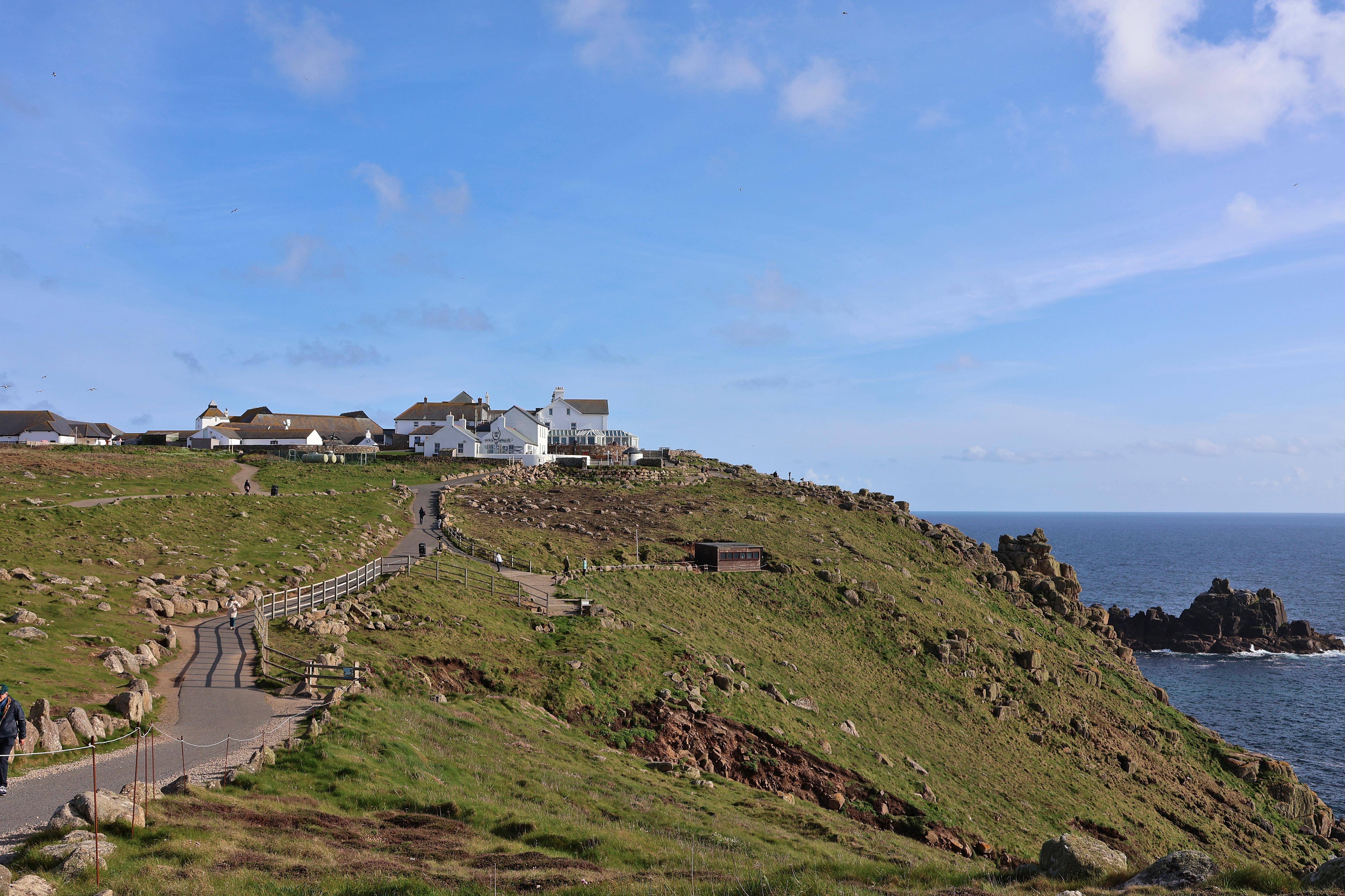 Idyllisk sommerbillede fra Land's End i Cornwall med grønne klippeformationer, stier og hvide bygninger ved den dramatiske atlanterhavskyst