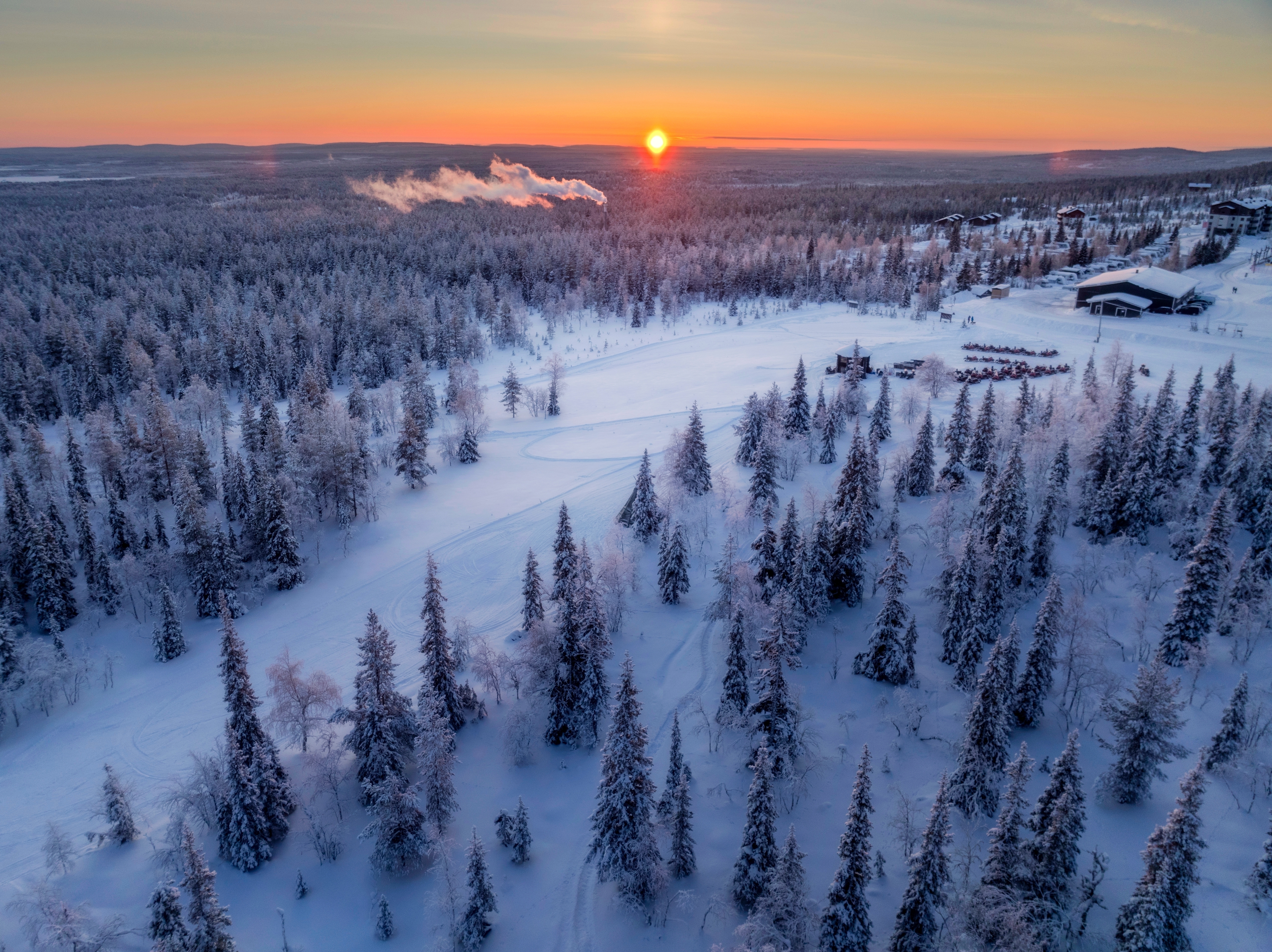 Eventyrligt vinterlandskab i Lapland med snedækkede træer og solnedgang der farver himlen i varme nuancer