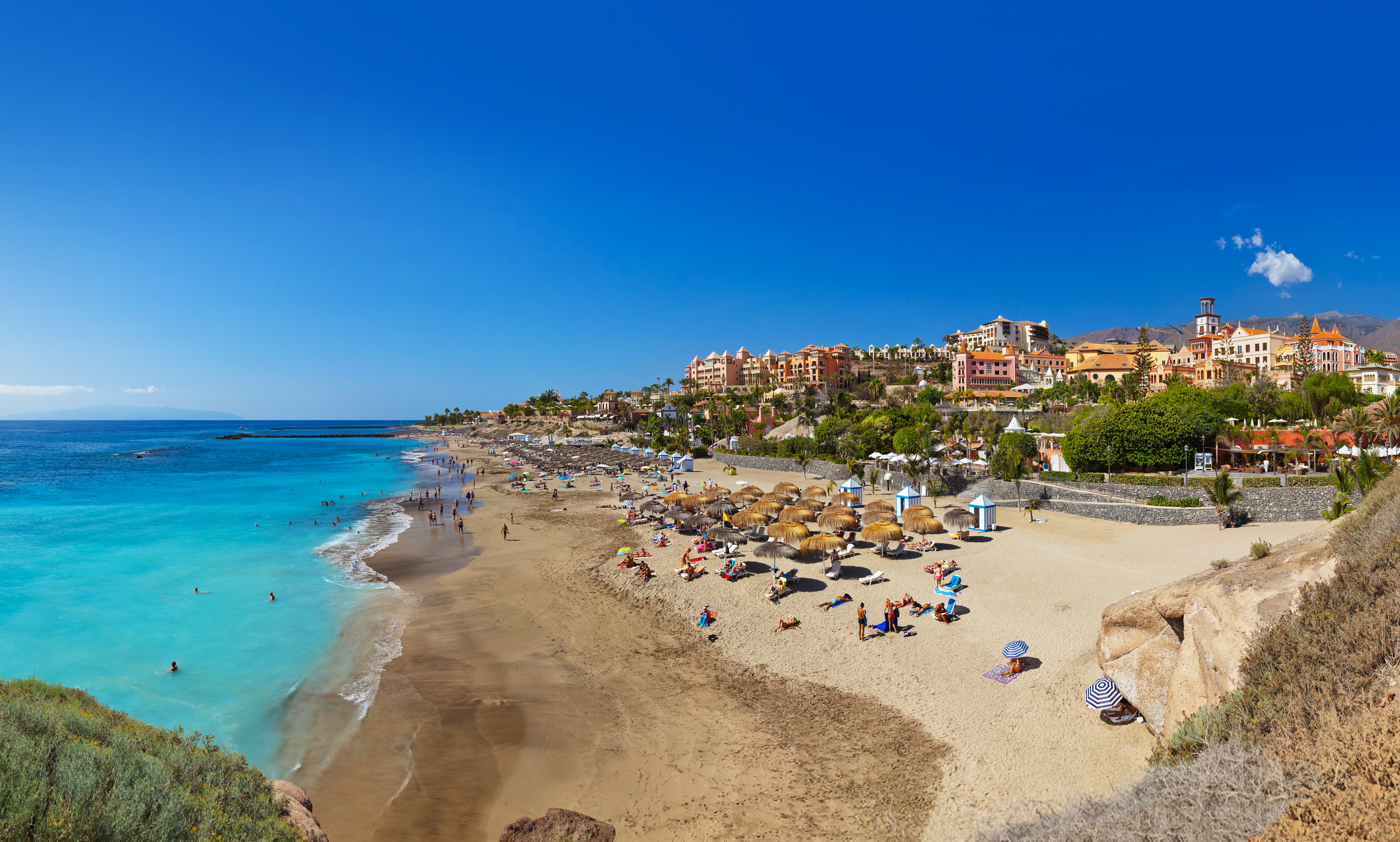 Idyllisk strandbillede fra Playa de Las Americas på Tenerife med turkist hav, stråparasoller og flotte feriehoteller i solskin