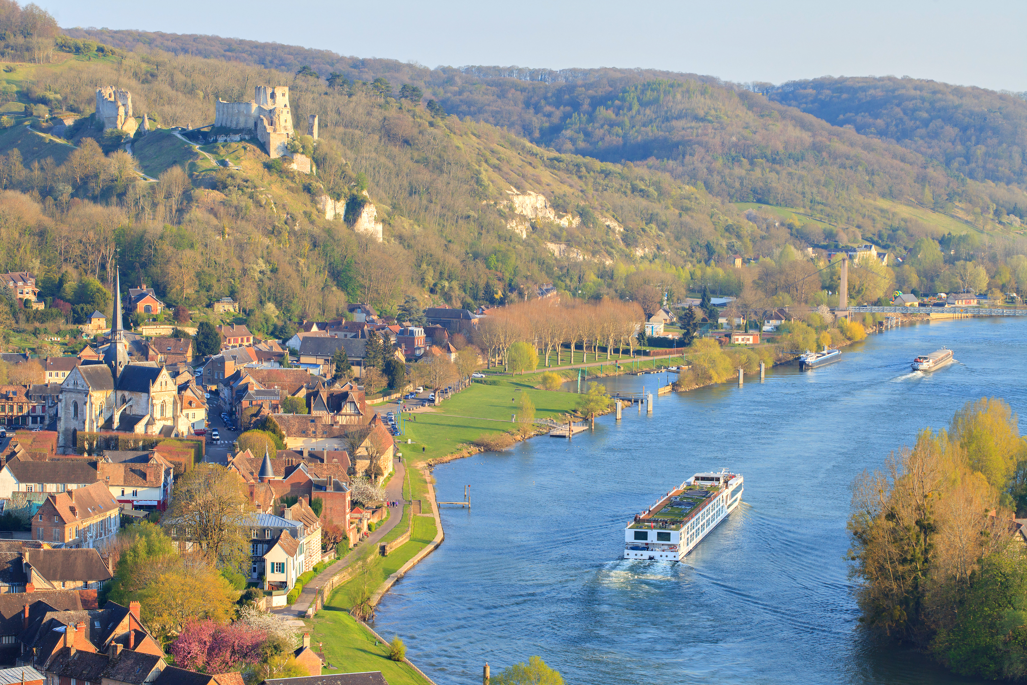 Idyllisk udsigt over Les Andelys og Seine-floden i Normandiet med et flodkrydstogtskib og de maleriske ruiner af Château Gaillard på bakketoppen