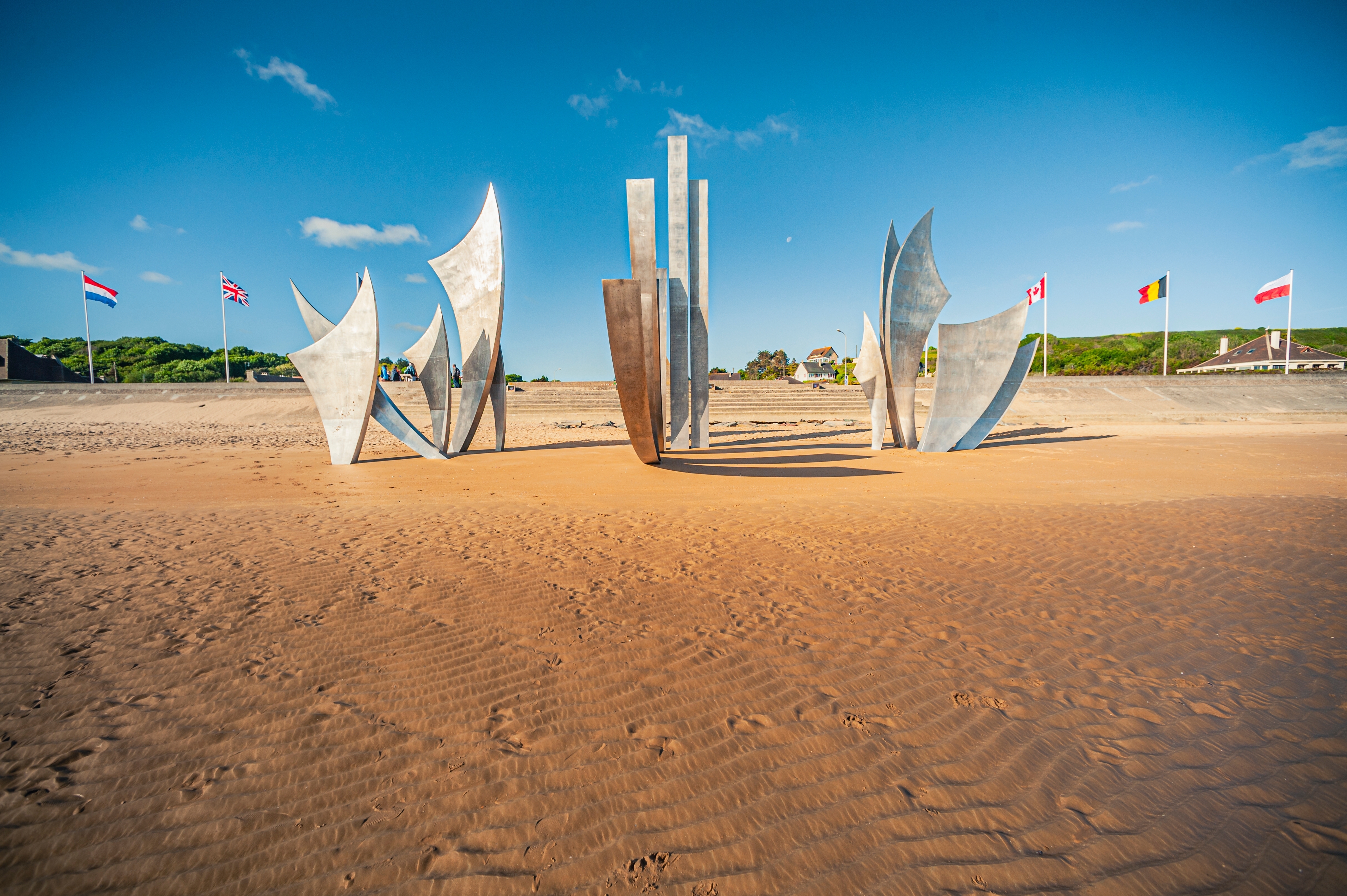 Skulpturmonumentet Les Braves på den historiske Omaha Beach i Normandiet, med allierede landes flag og blå himmel