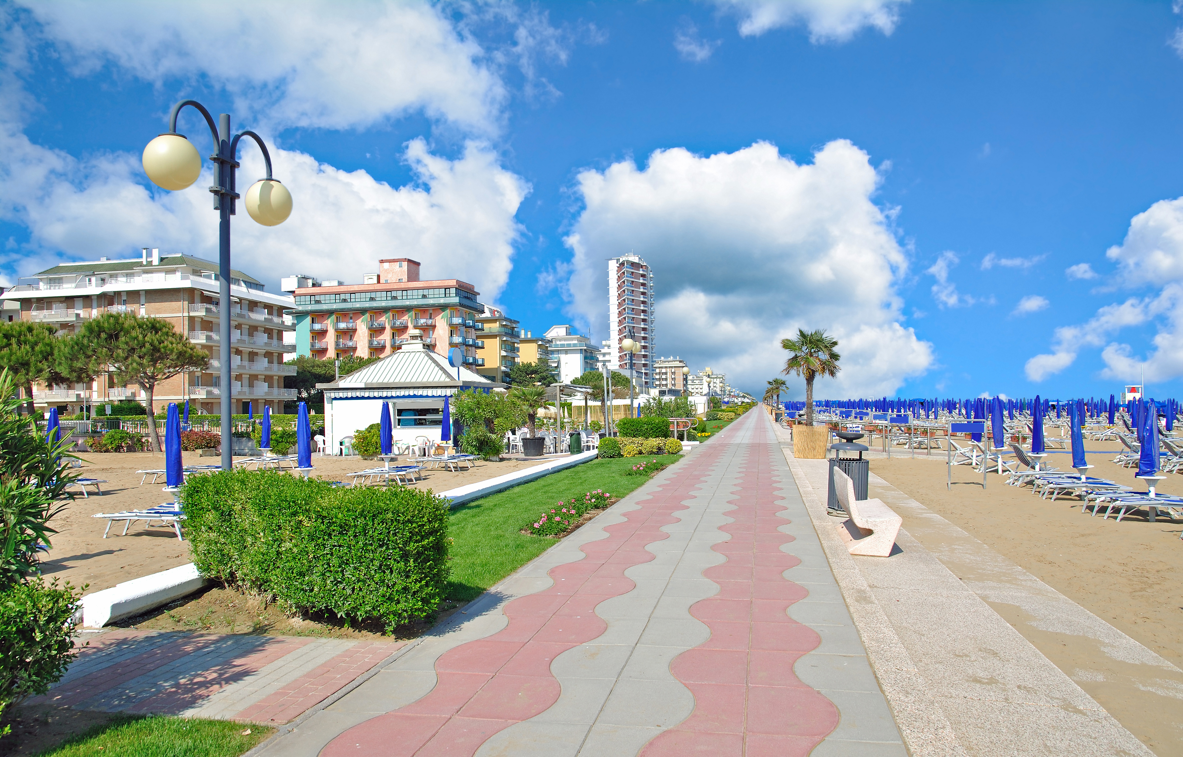 Solrig sommerdag på promenaden ved Lido di Jesolo med blå strandparasoller og liggestole langs Adriaterhavet i det nordlige Italien