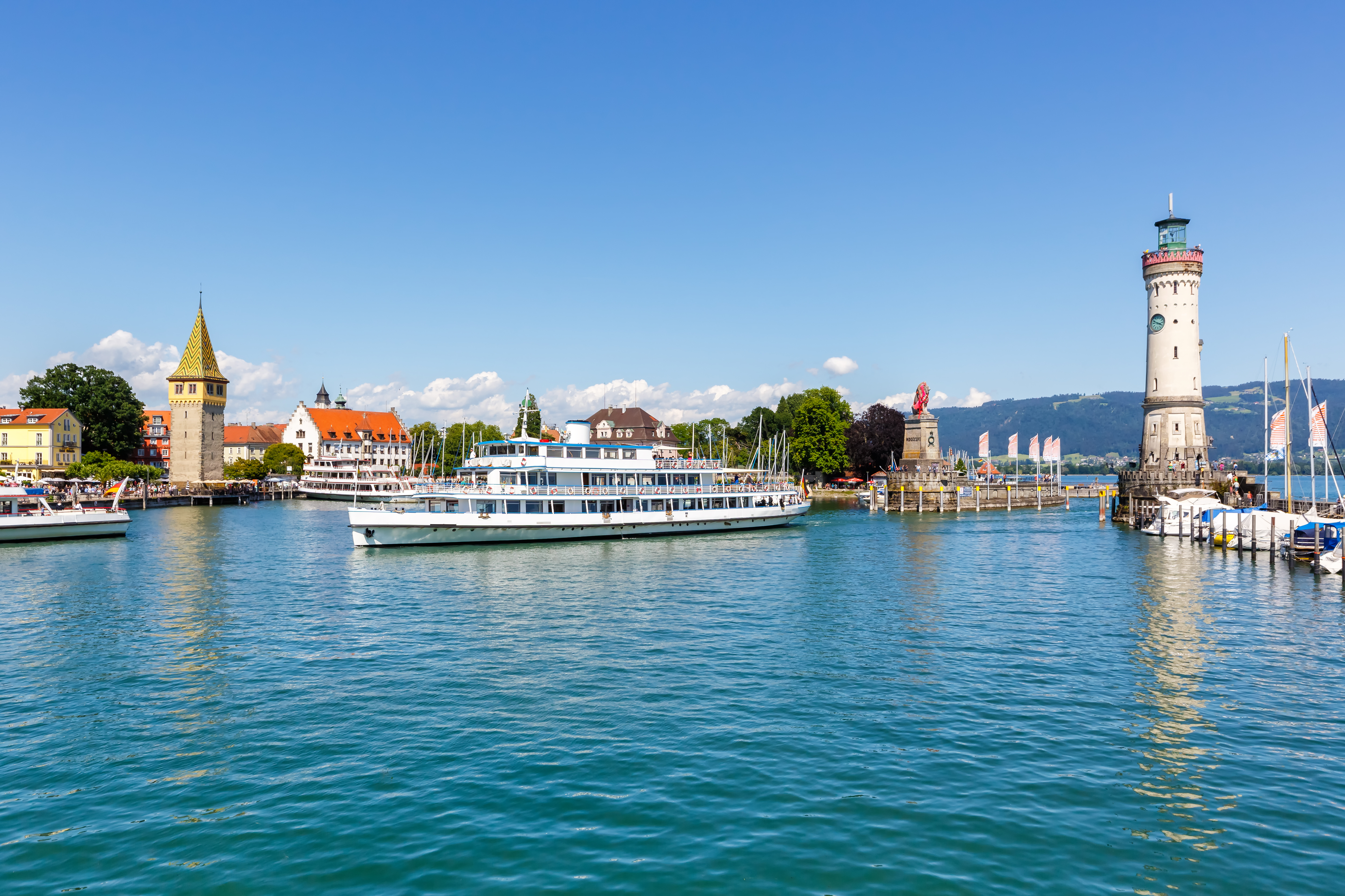 Lindau havn ved Bodensøen med hvid passagerfærge der sejler ind i marinaen, historisk fyrtårn og middelalderlig bybaggrund i Bayern