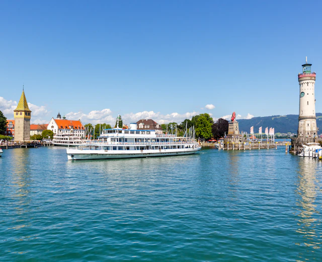 Lindau havn ved Bodensøen med hvid passagerfærge der sejler ind i marinaen, historisk fyrtårn og middelalderlig bybaggrund i Bayern