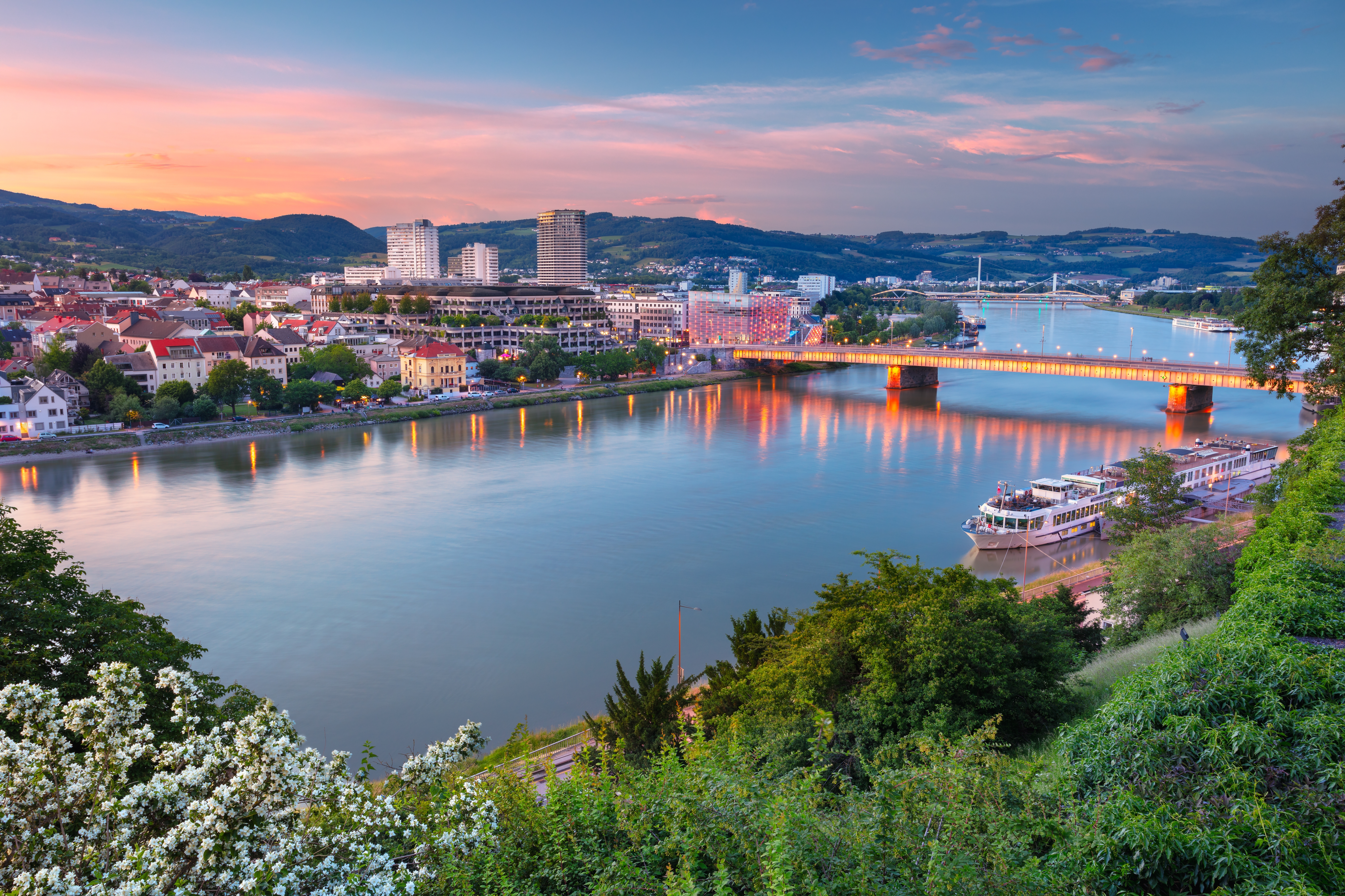 Imponerende luftbillede af Linz ved Donau, hvor aftensolens sidste stråler og byens lys skaber en fortryllende stemning