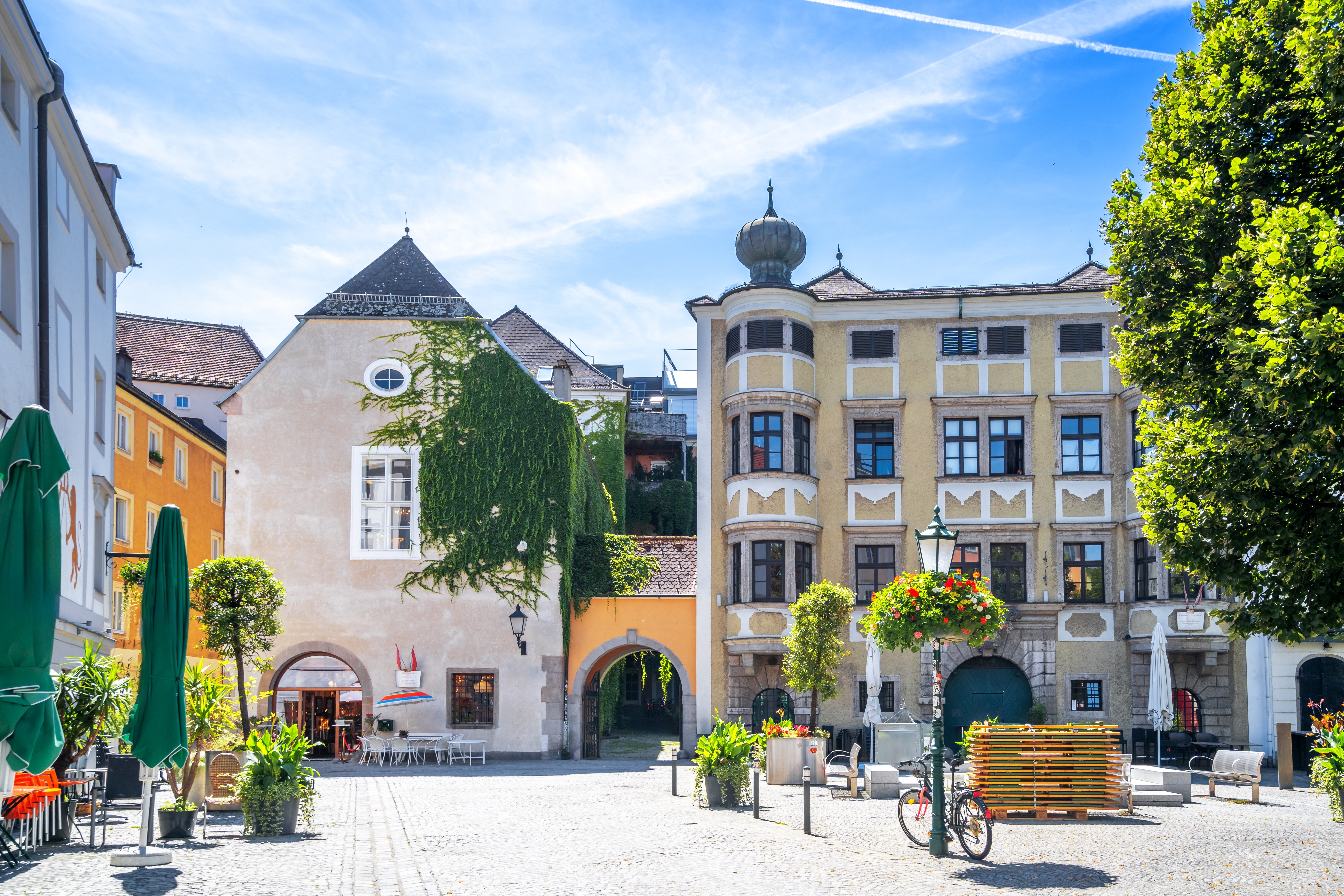 Solrig sommerdag på det brolagte torv i Linz med historiske gule bygninger, grønne træer og blomsterpynt i Østrigs næststørste by