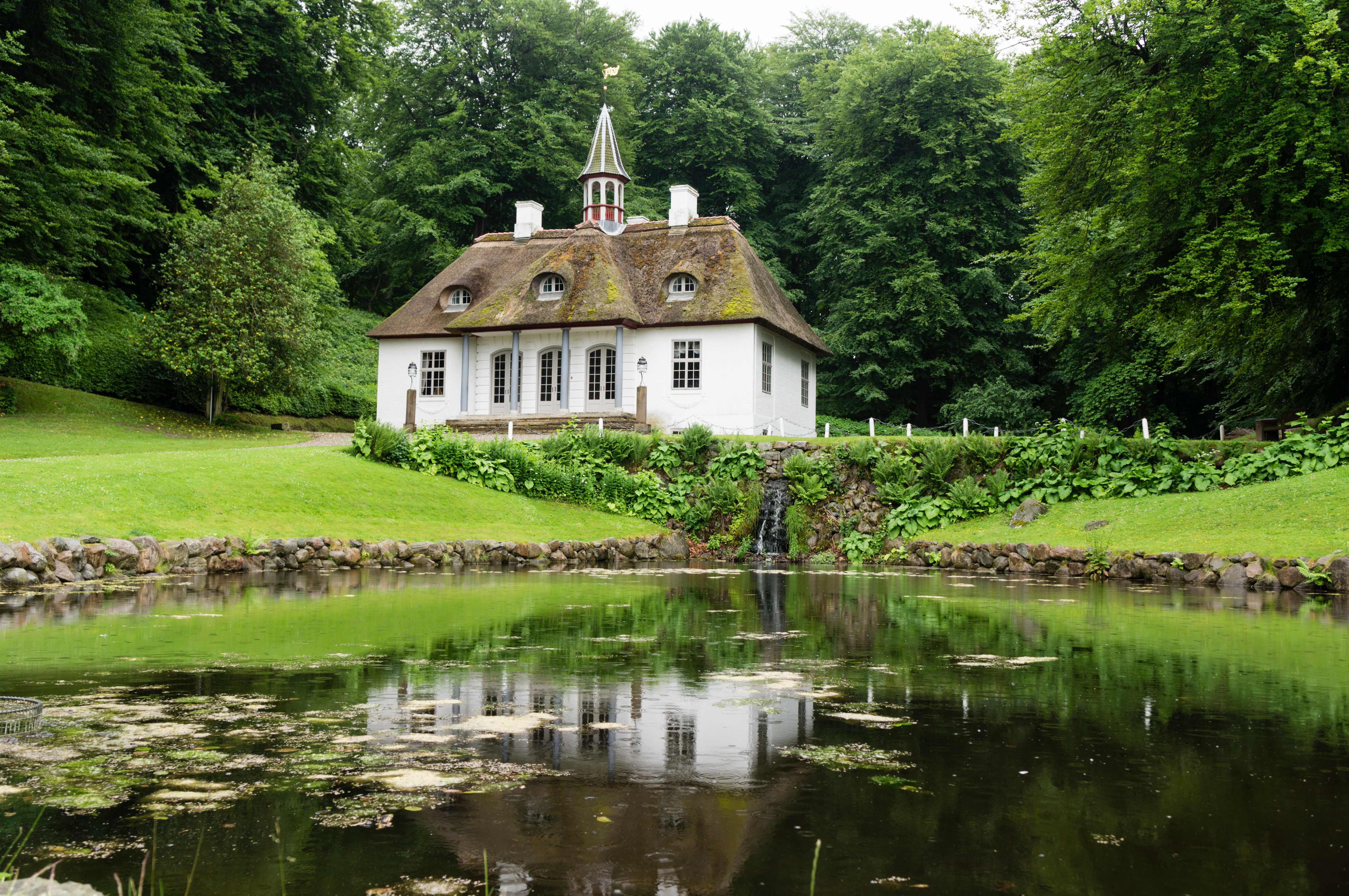 Naturskønt Liselund Slot på Møn omgivet af fredfyldt skov og spejlet i en stille dam med åkander