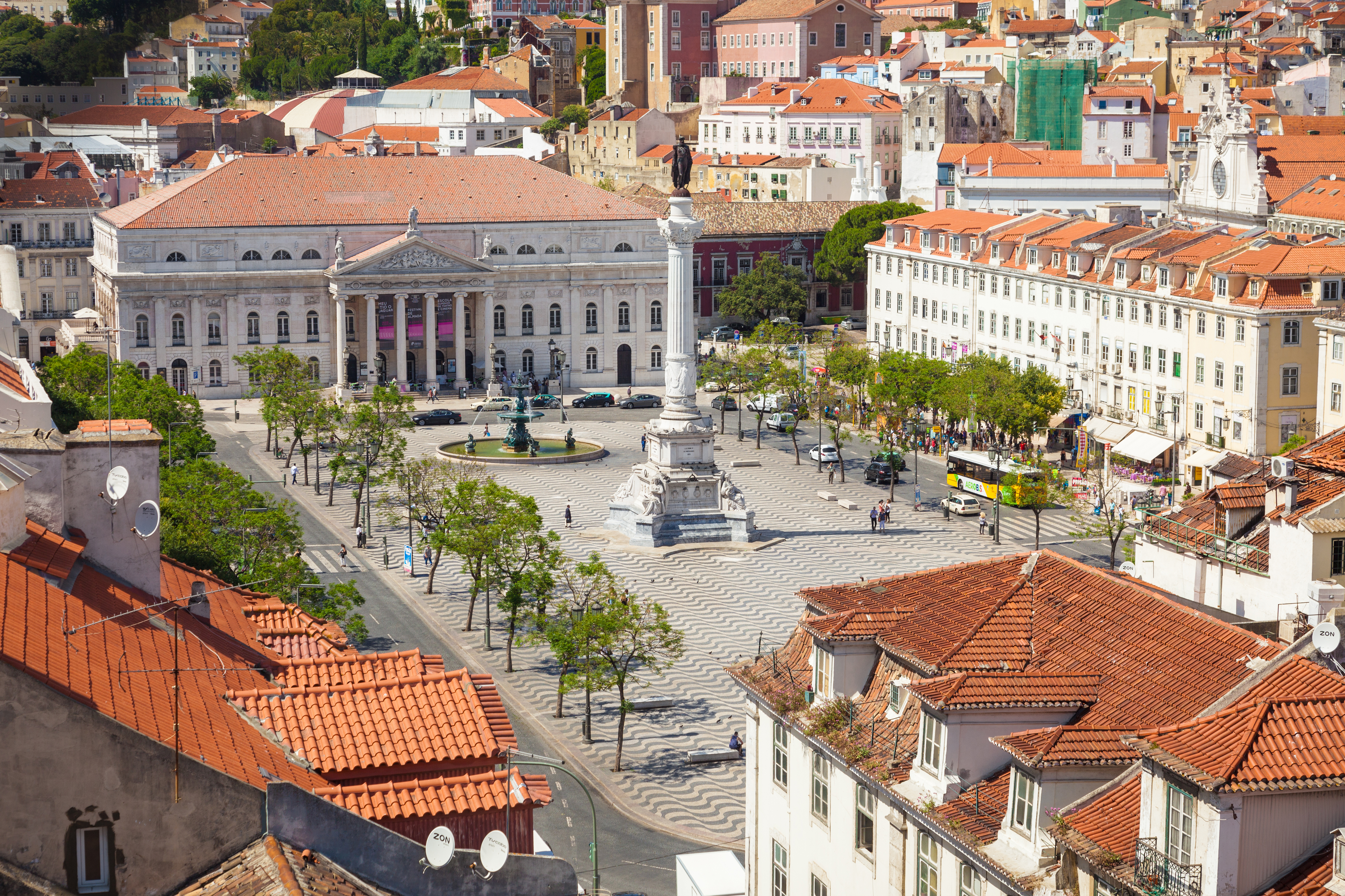 Luftfoto af Rossio-torvet i Lissabon med det smukke bølgemønster i brostenene, Dom Pedro IV-monumentet og Nationaltheatret omgivet af røde tage