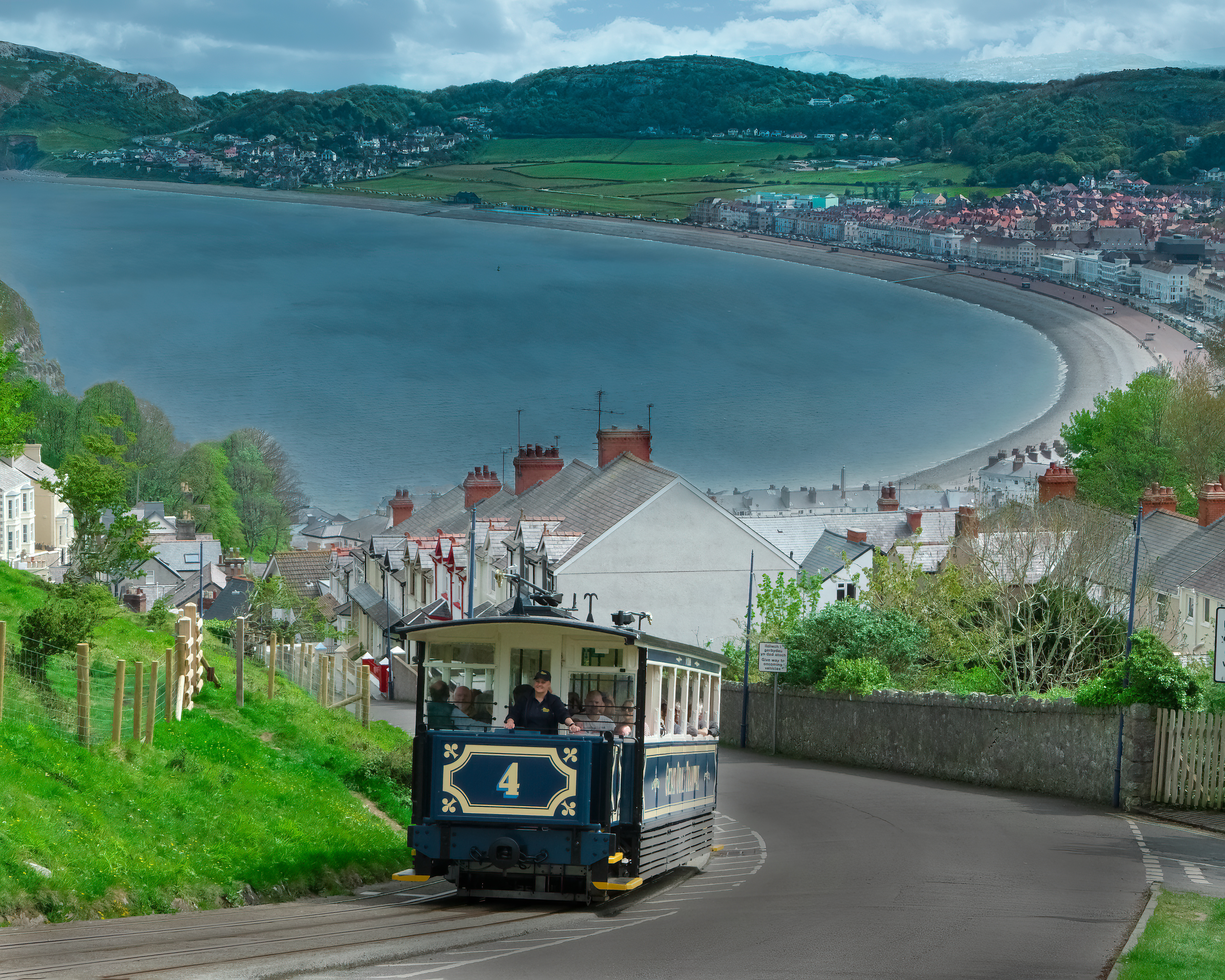 Den ikoniske Great Orme-sporvogn i Llandudno, Wales, kører op ad bakken med den pittoreske bugt og strandpromenade i baggrunden