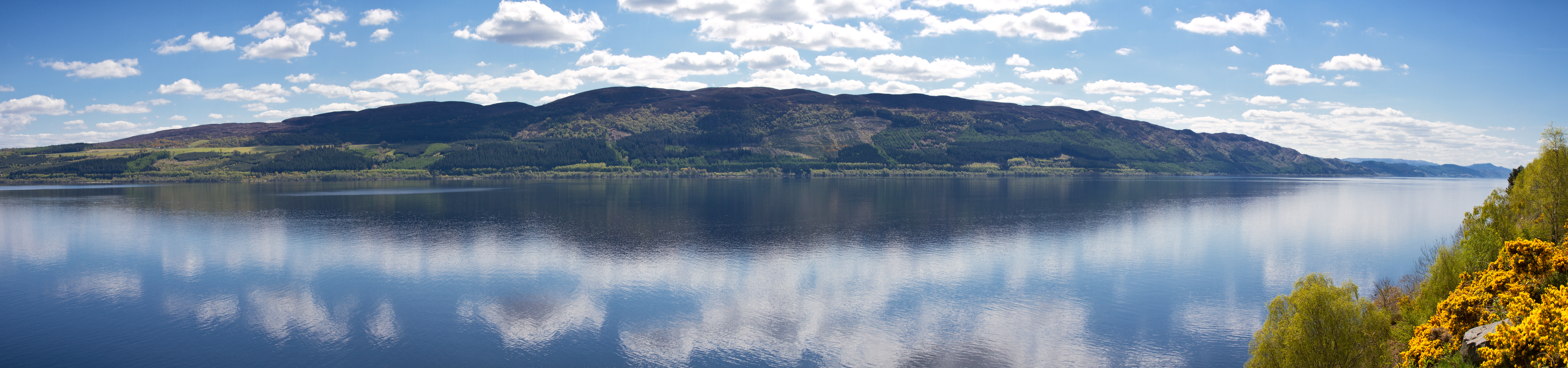 Panoramaudsigt over Loch Ness med spejlblankt vand og dramatiske skyer over de skotske højlande