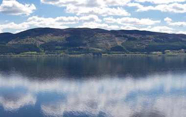 Panoramaudsigt over Loch Ness med spejlblankt vand og dramatiske skyer over de skotske højlande