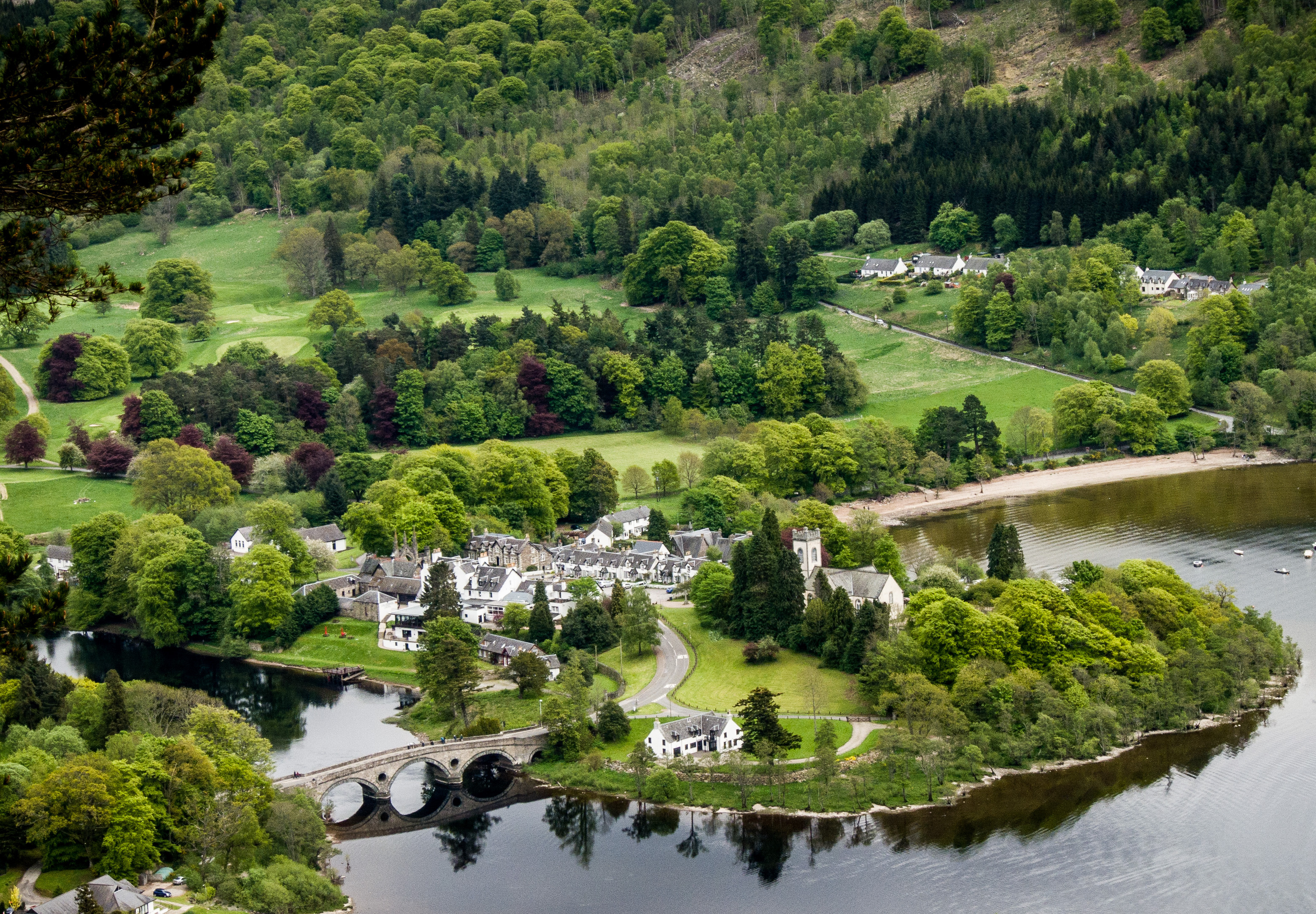 Luftfoto af Kenmore ved Loch Tay i de skotske Highlands med frodig grøn natur, historisk bro og malerisk landsby