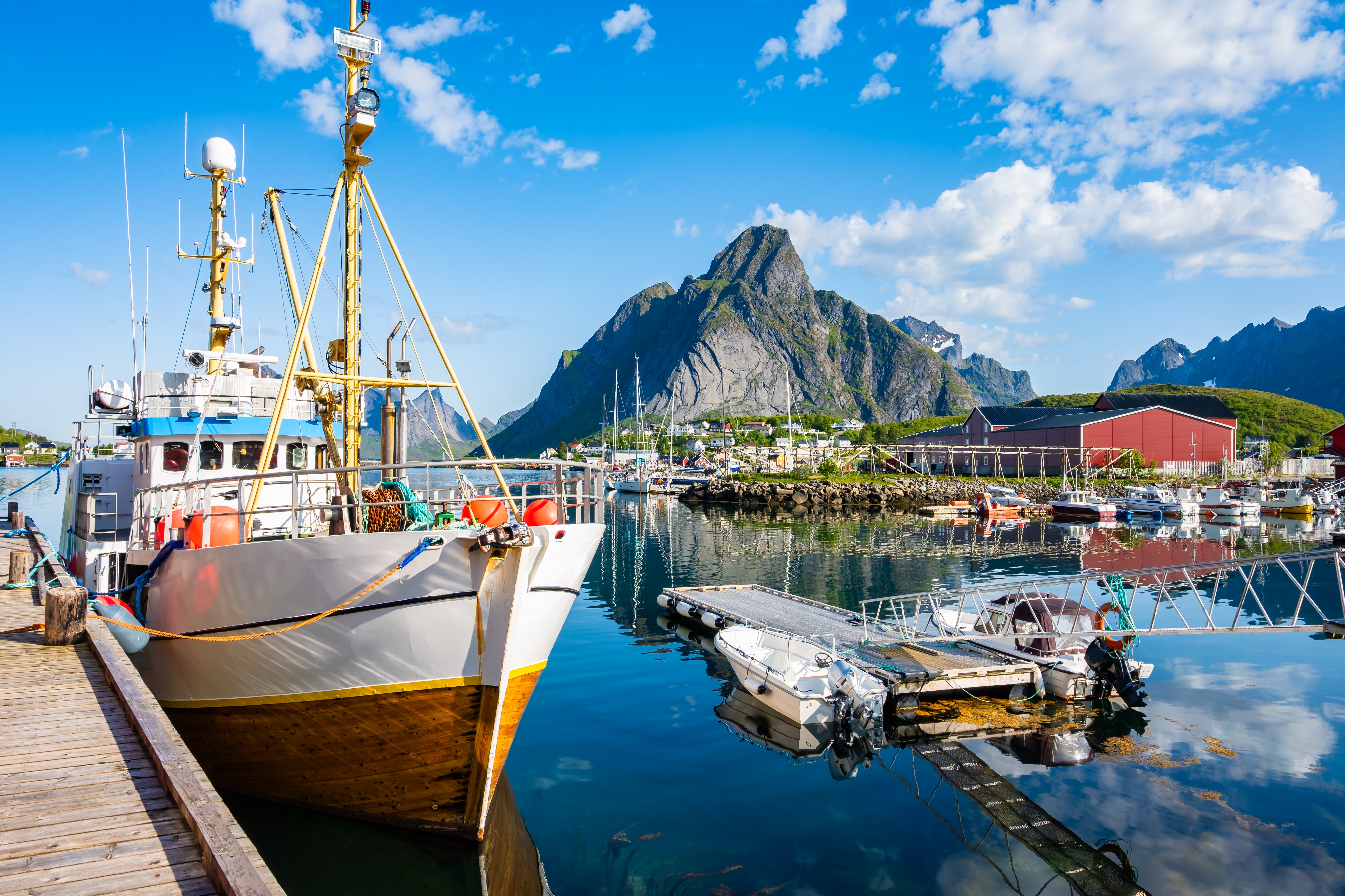 Smuk sommerdag i Reine på Moskenesøy, Lofoten, med fiskerbåde i havnen og karakteristiske norske bjerge spejlet i fjorden