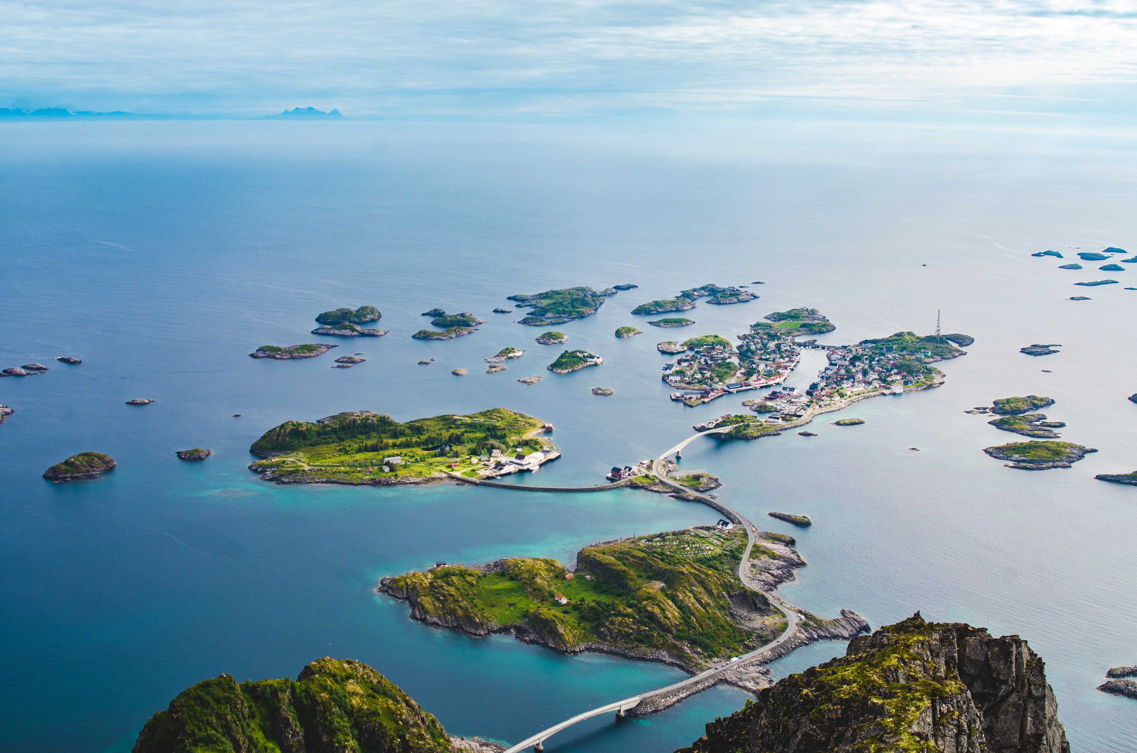 Fugleperspektiv over Henningsvær på Lofoten i Norge, med grønne øer forbundet af broer i det klare turkisblå nordatlantiske hav