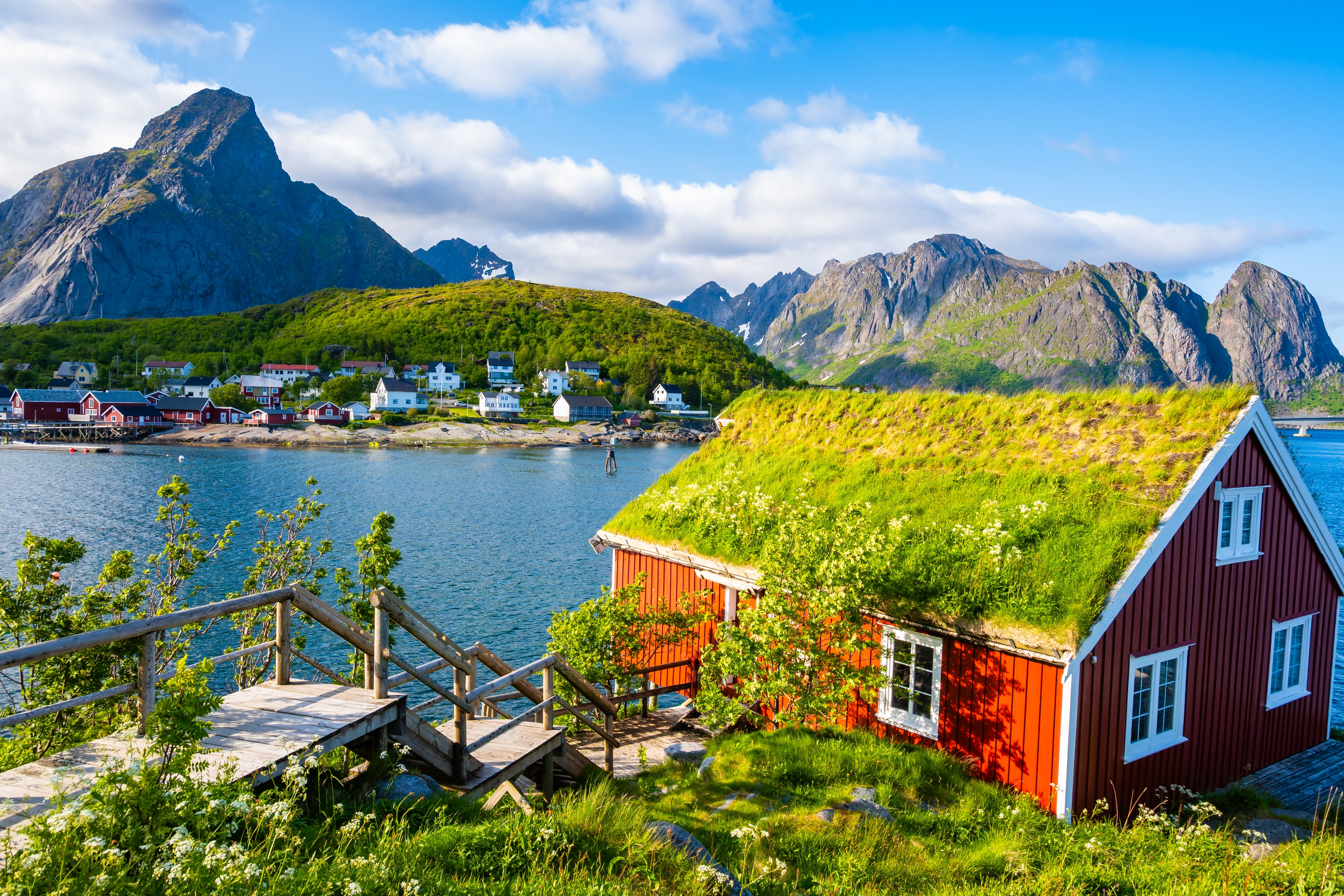 Traditionel rød norsk rorbu med græstag i Reine på Lofoten med panoramaudsigt over fjord og dramatiske bjergtoppe