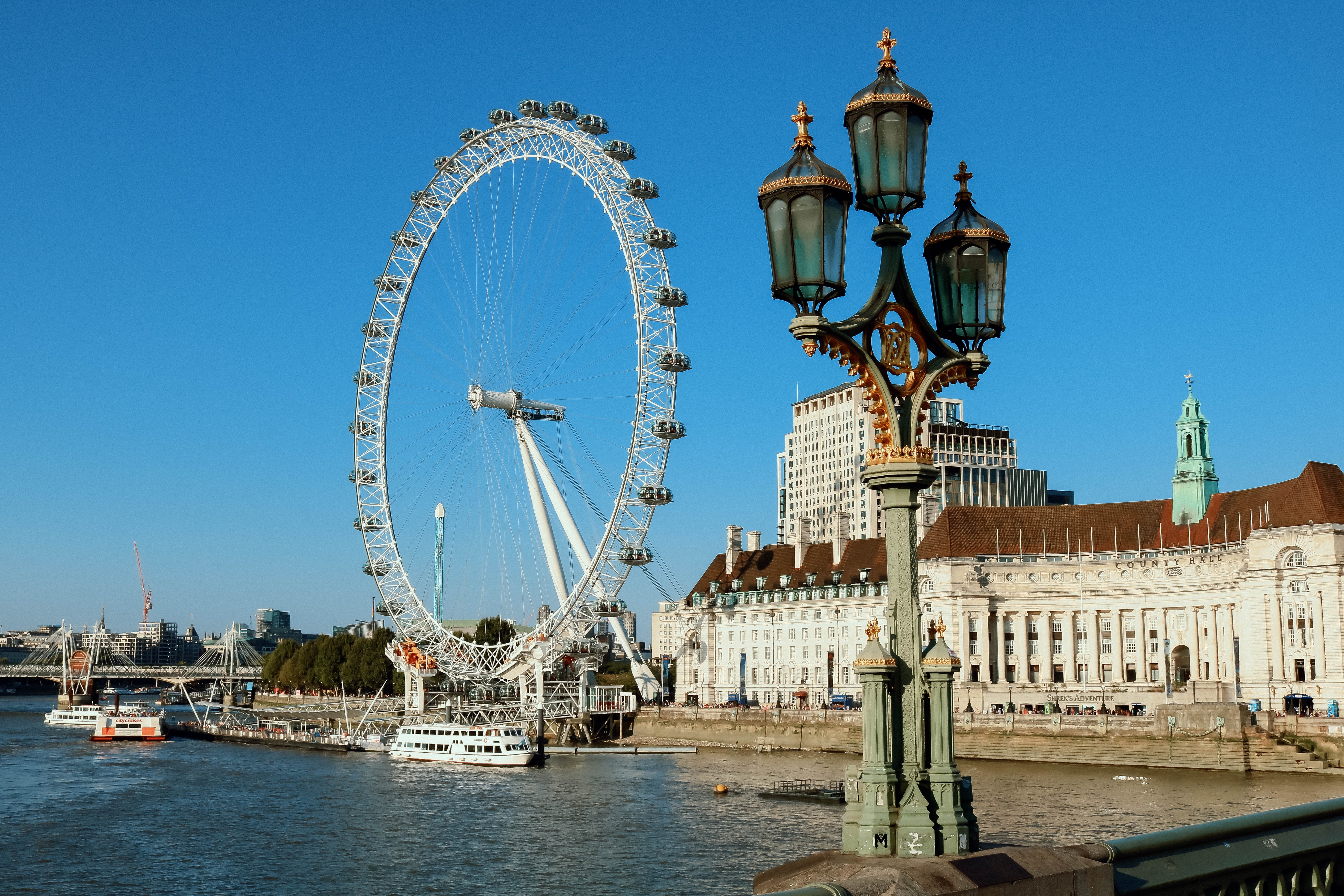 London Eye pariserhjulet set fra Westminster Bridge med klassisk victoriansk lygtepæl og blå himmel over Themsen