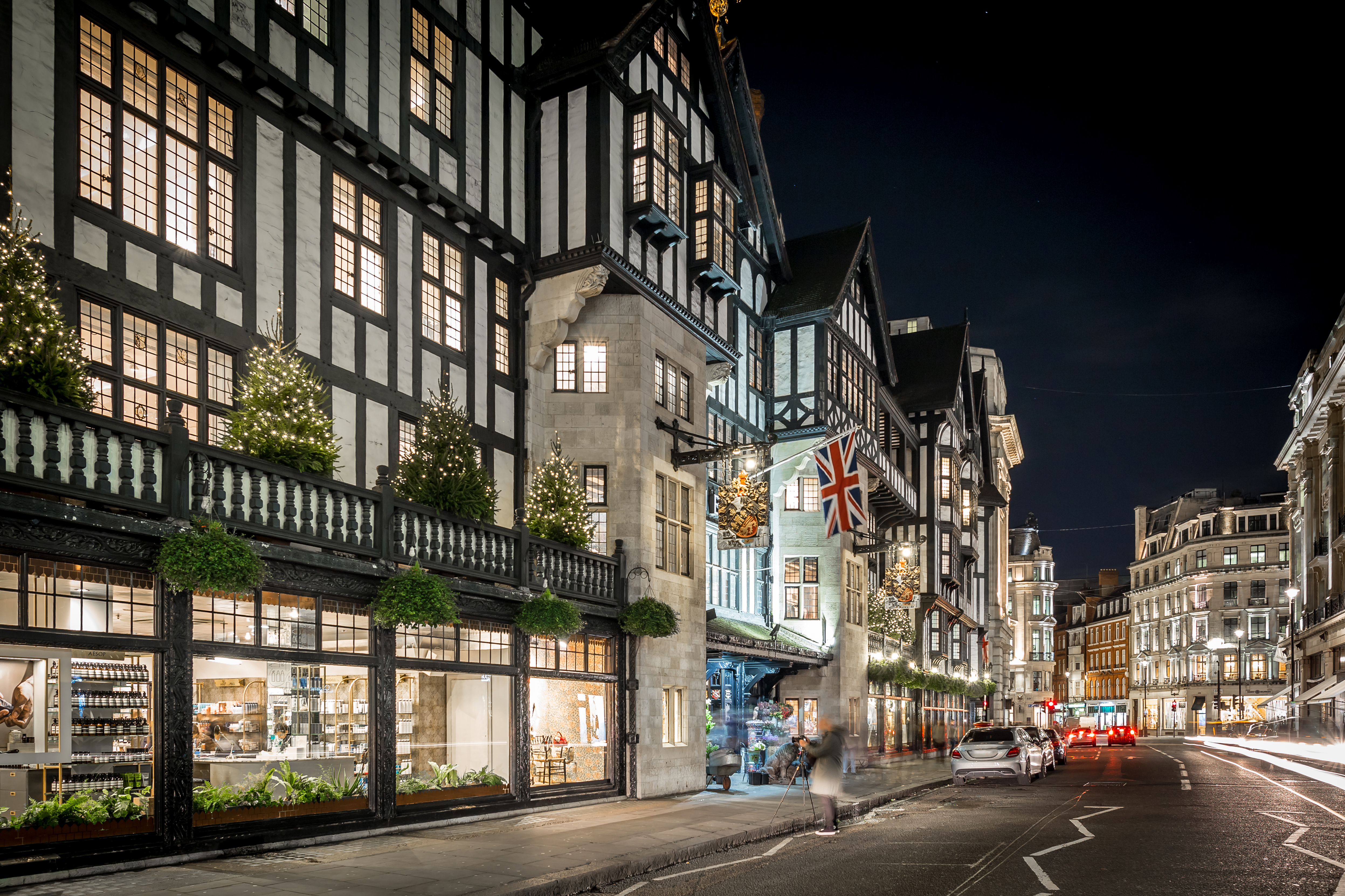 Juleoplevelse ved Liberty London varehus med funklende julelys og Union Jack flag om natten i hjertet af London