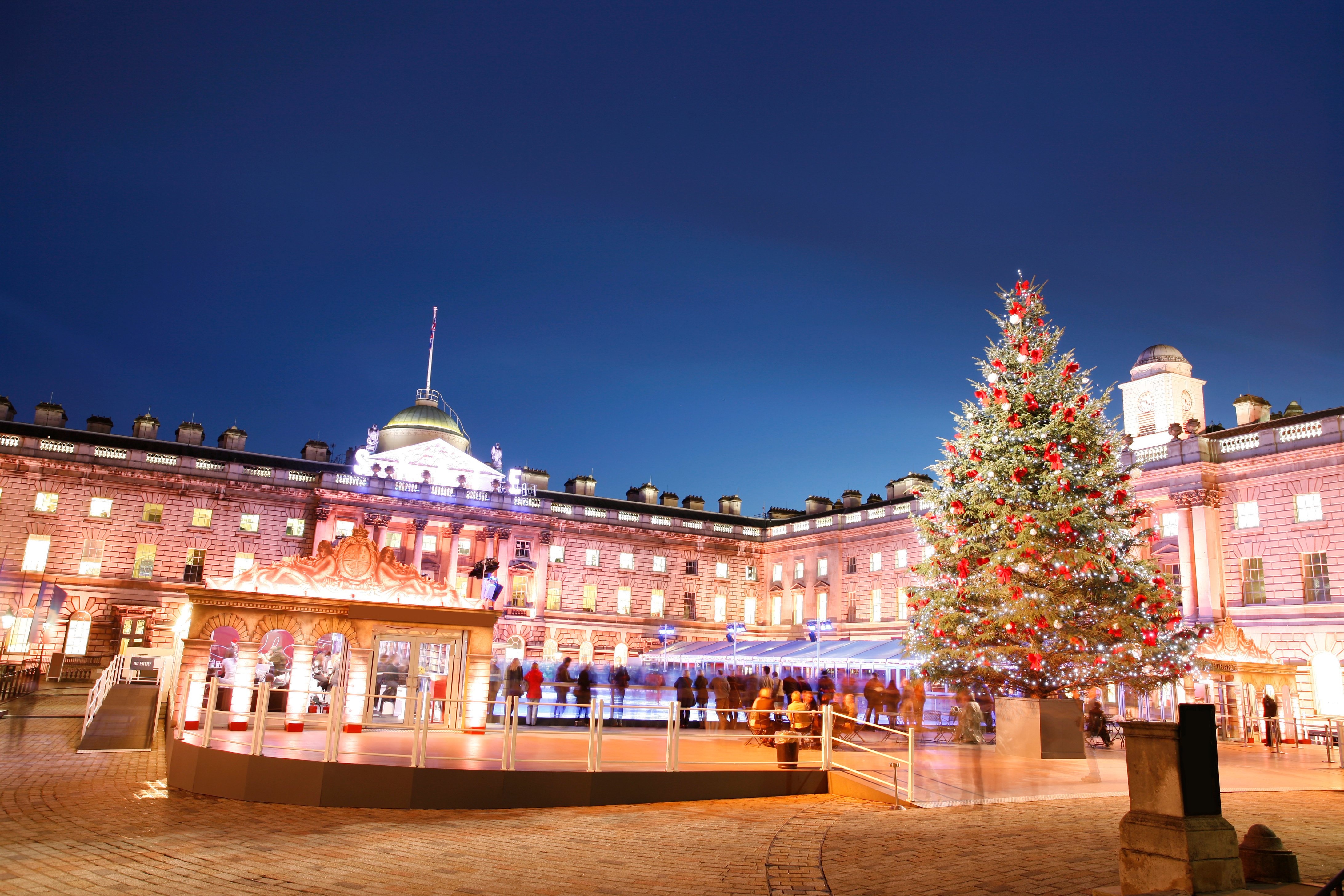 Julestemning ved Somerset House i London med oplyst facade, issbane og flot dekoreret juletræ i vintermørket