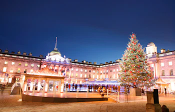 Julestemning ved Somerset House i London med oplyst facade, issbane og flot dekoreret juletræ i vintermørket