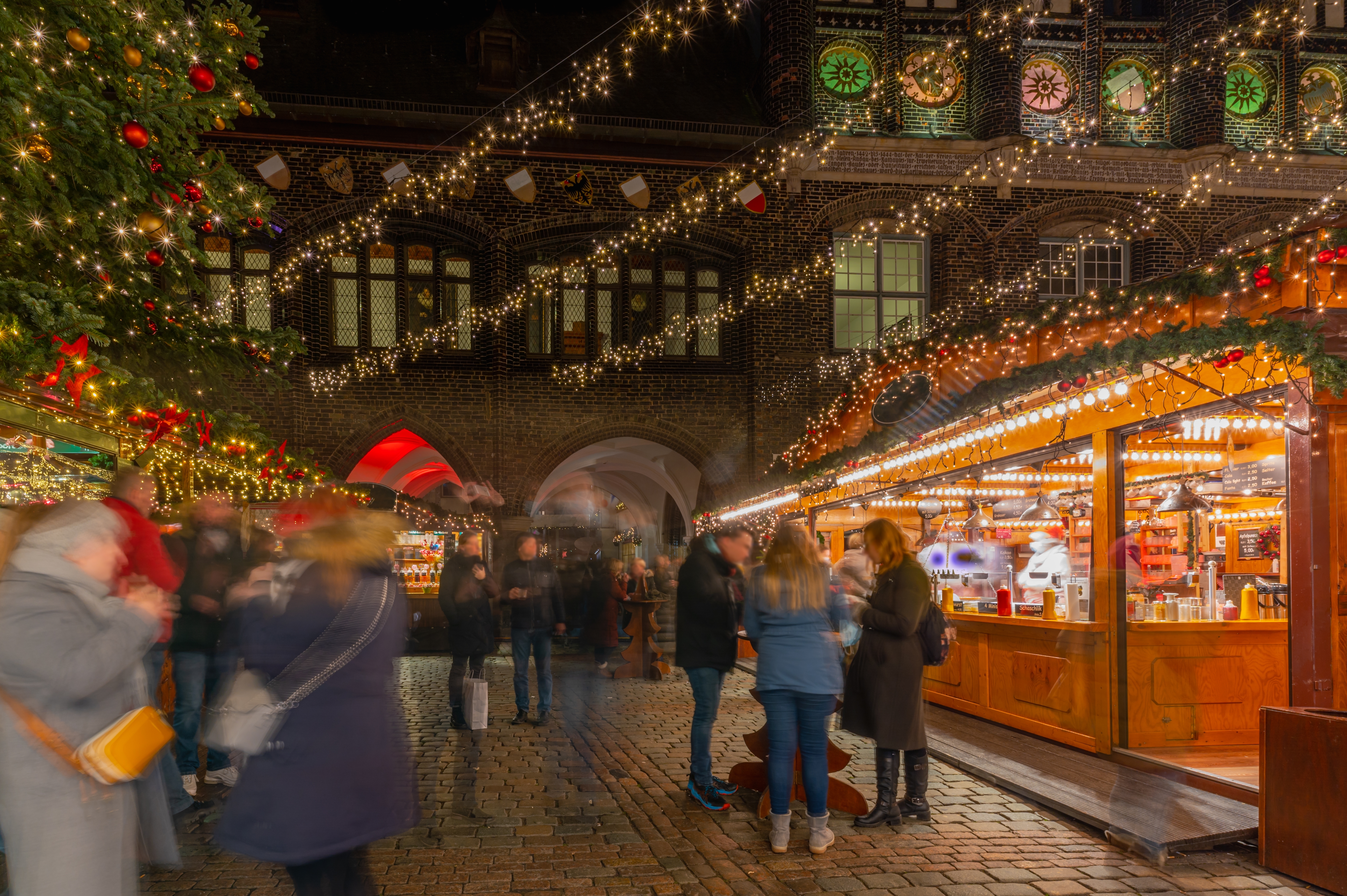 Magisk julestemning på julemarkedet i Lübeck, Tyskland, med varmt oplyste træboder, julepynt og gæster i den historiske midtby om natten