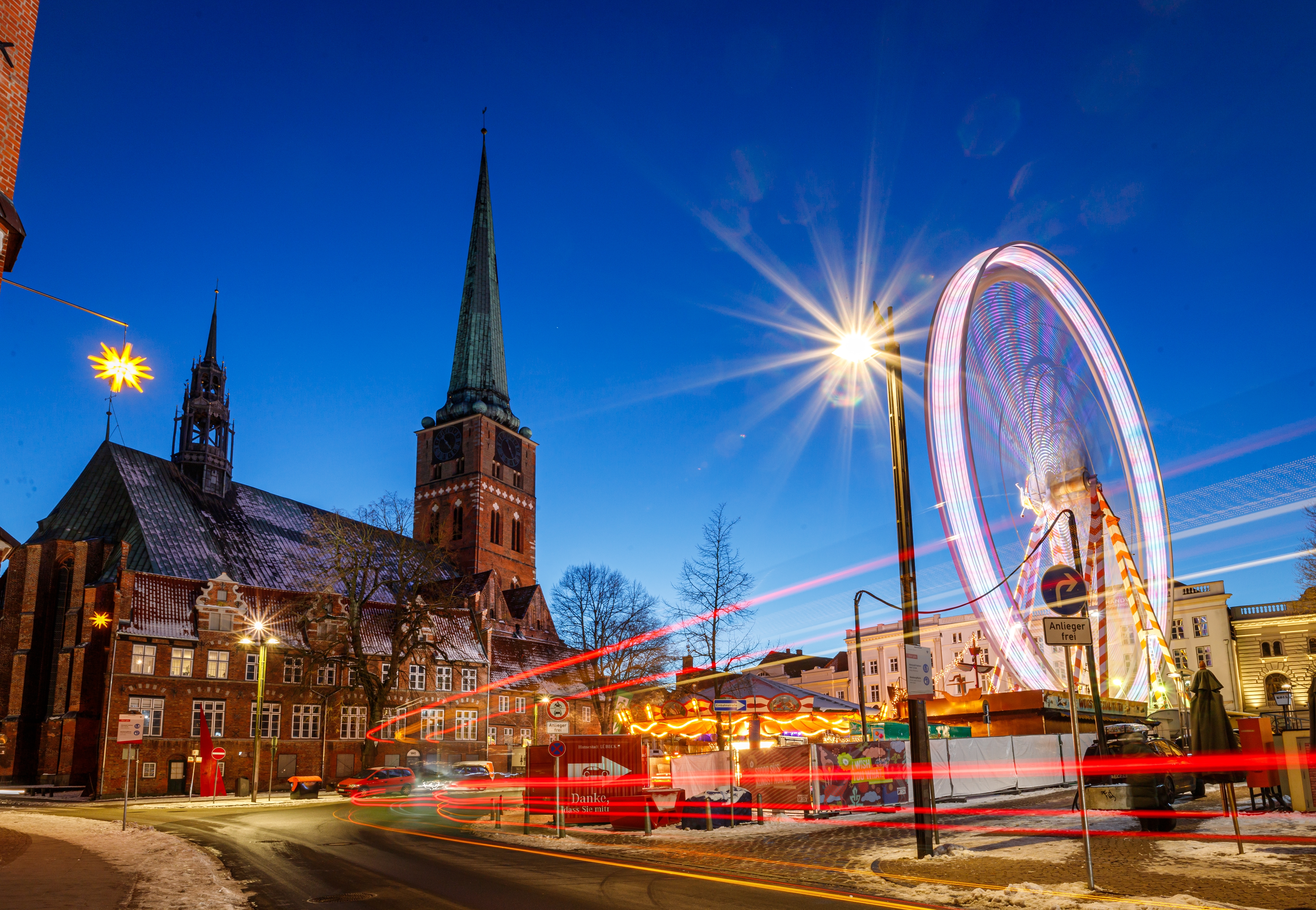Festligt julemarked i Lübeck med farverigt pariserhjul og imponerende gotisk kirke i blå time