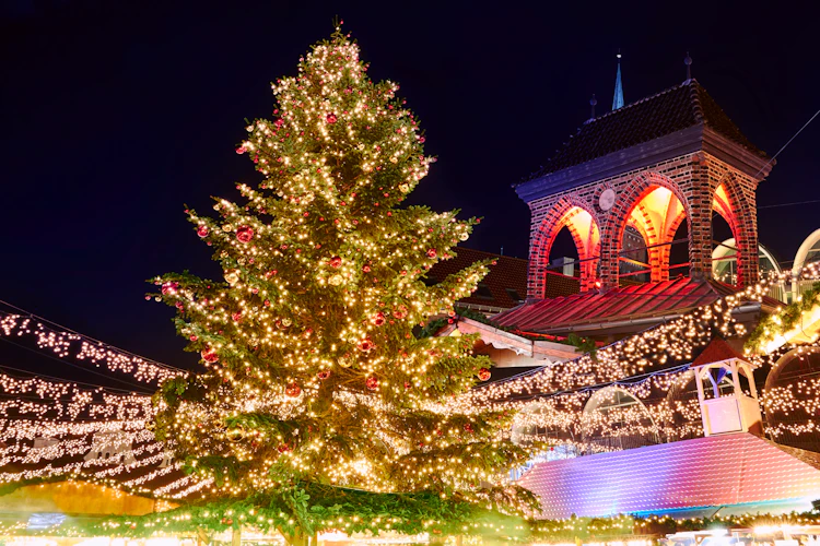 Smukt dekoreret juletræ med røde ornamenter og hvide lys på det traditionelle julemarked i Lübeck om natten