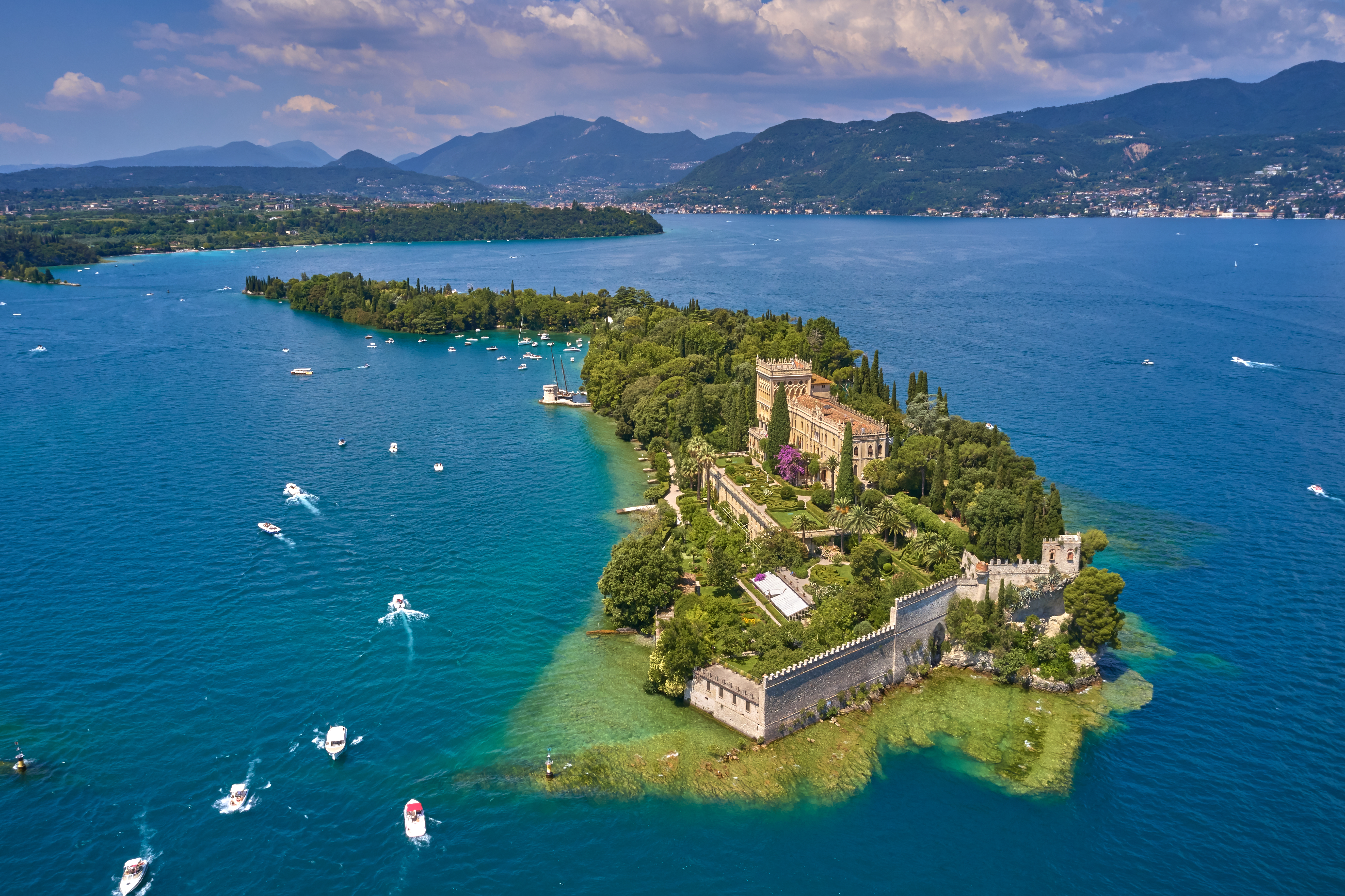 Panoramaudsigt fra luften over Isola del Garda på Gardasøen i Italien med den historiske villa, grønne haver, sejlbåde og de majestætiske alper som naturlig baggrund