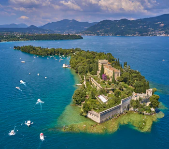Panoramaudsigt fra luften over Isola del Garda på Gardasøen i Italien med den historiske villa, grønne haver, sejlbåde og de majestætiske alper som naturlig baggrund