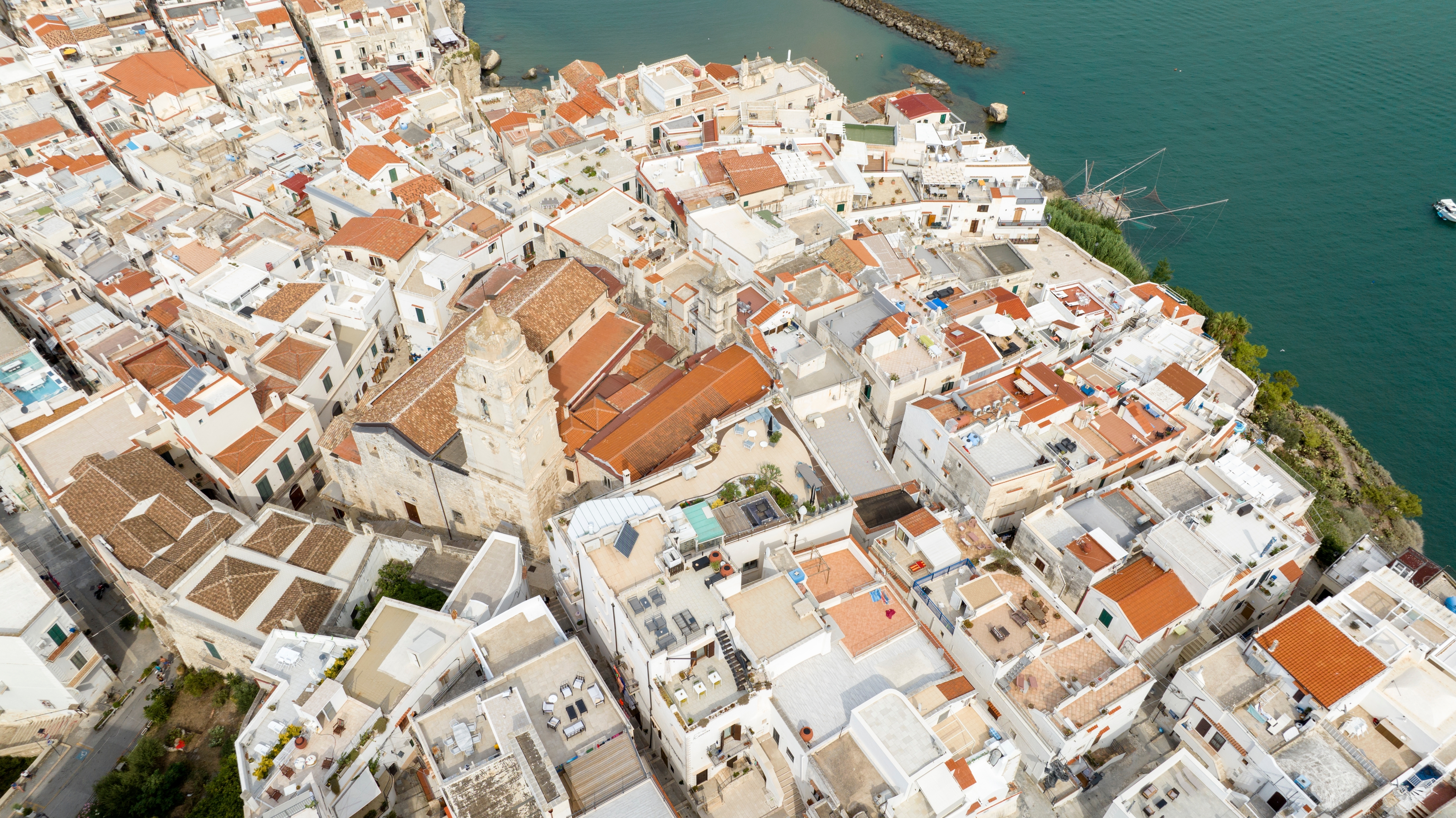 Smukt luftfoto af Vieste i det sydlige Italien med tæt liggende hvide huse, terrakottatage og en imponerende katedral ud mod havet