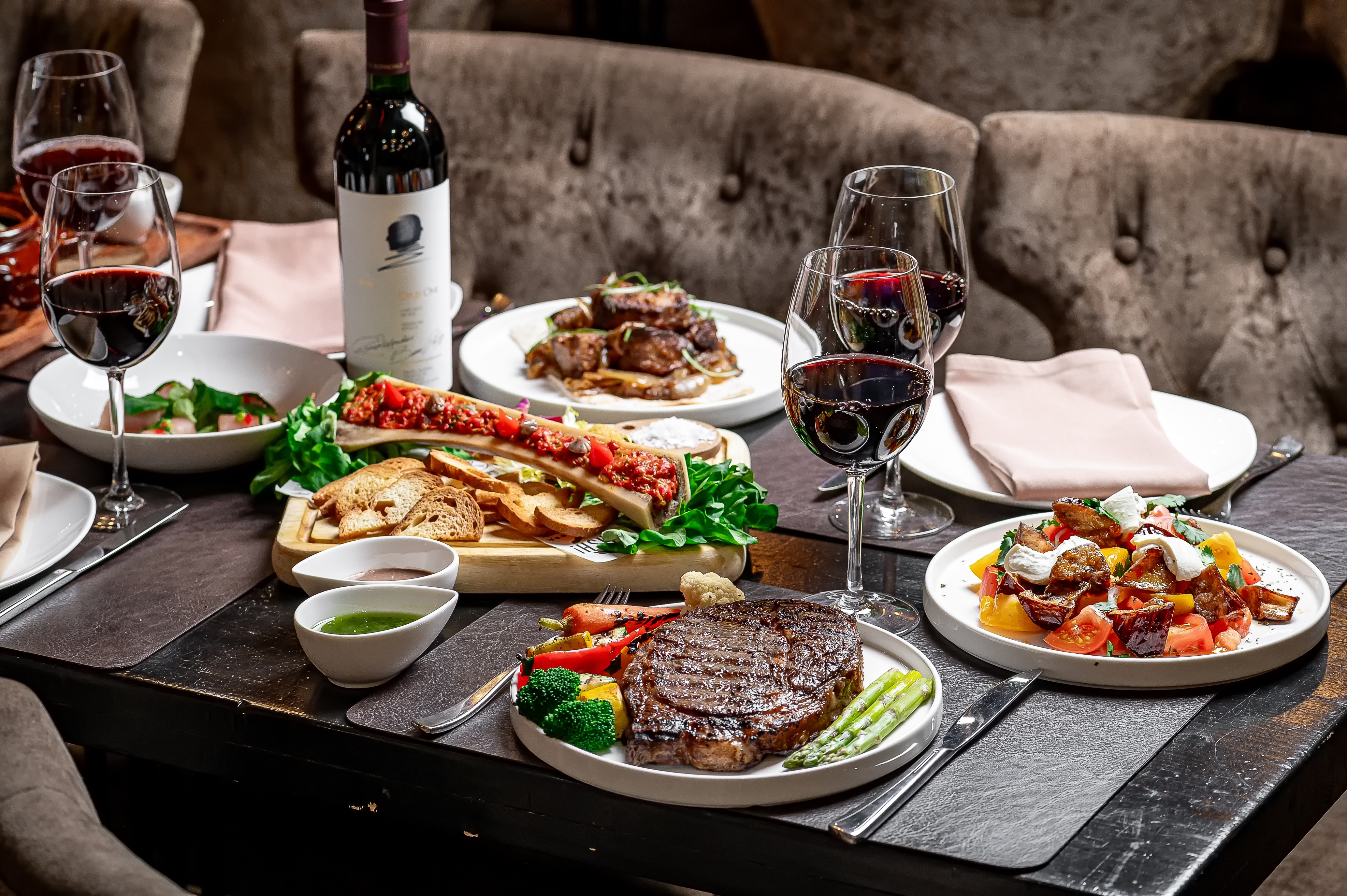 Festlig restaurantmiddag med grillet ribeye bøf, dampede grøntsager, charcuteri og fyldte glas rødvin på et elegant steakhouse