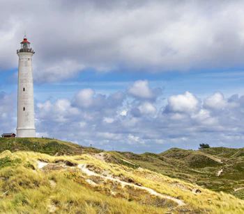 Udsigt til det historiske Lyngvig Fyr fyrtårn ved Hvide Sande med grønne klitter og blå himmel på Jyllands vestkyst