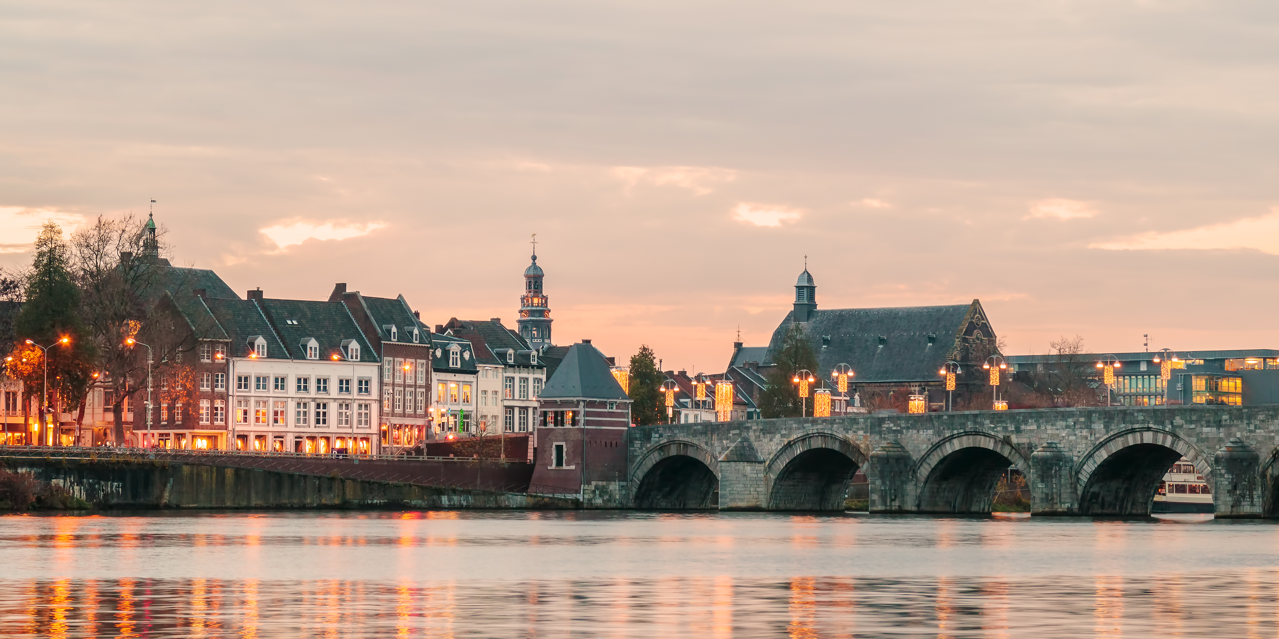 Idyllisk solnedgang over Sint Servaas-broen og den historiske bymidte i Maastricht med refleksioner i Maas-floden
