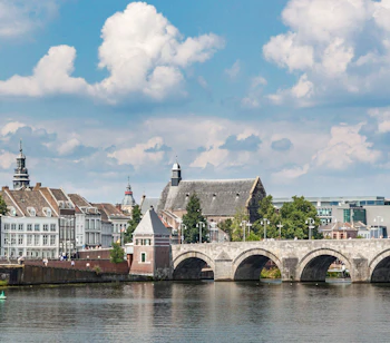 Stenbroen over floden med traditionelle hollandske bygninger og kirketaarne i Maastricht