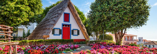 Historiske trekantede hytter med stråtag og farverige facader omgivet af blomster i Santana på Madeira-øen