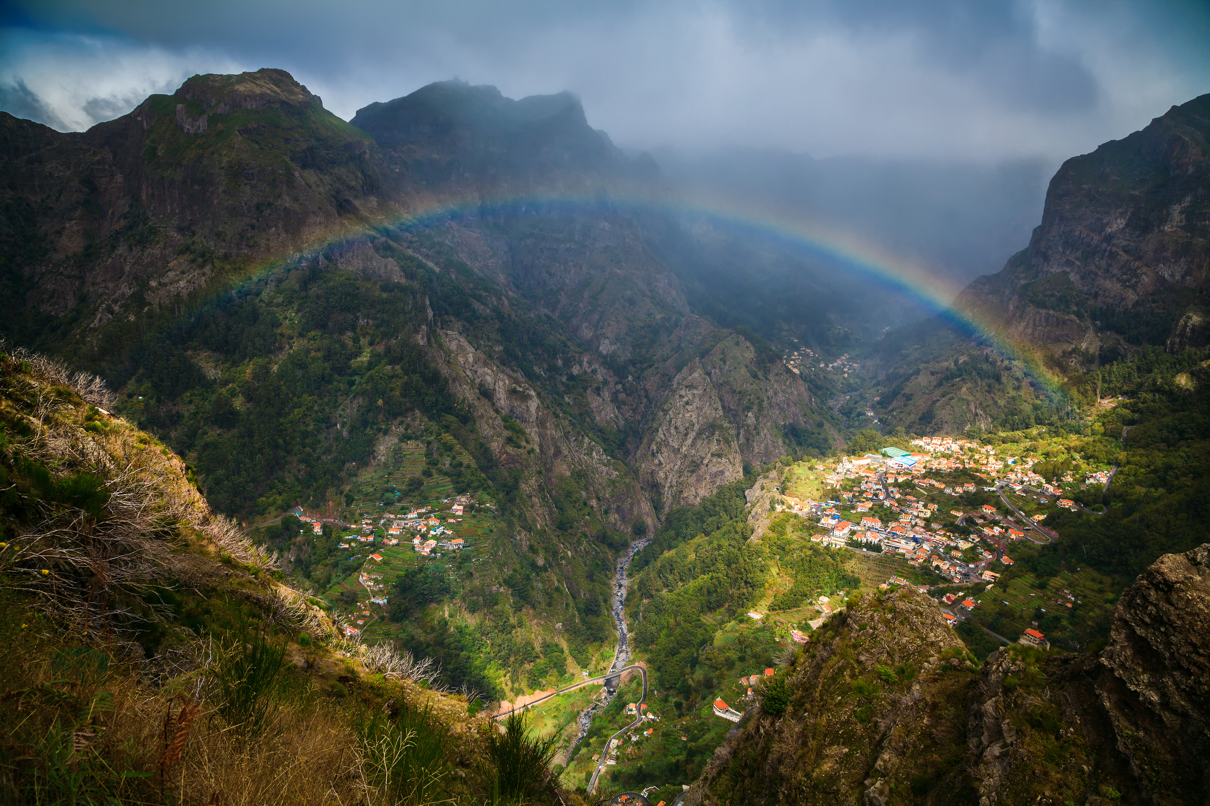 Naturskøn regnbue over bjerglandsby på Madeira med grønne dale og vulkanske bjerge
