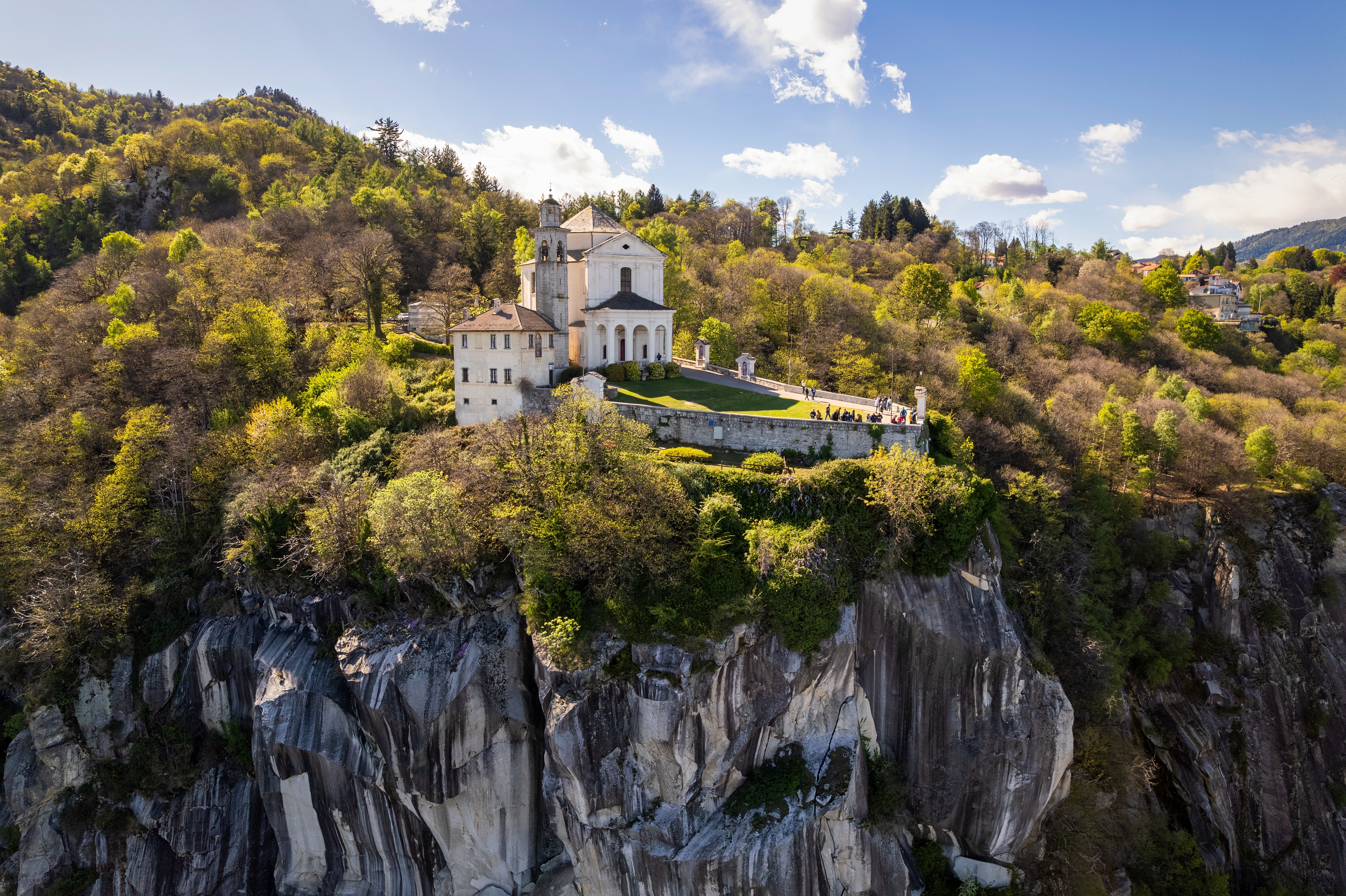Drone-foto af det smukke og historiske Madonna del Sasso-sanktuarium, der troner på en dramatisk klippeskrænt med skovdækkede bakker i Piemonte, Norditalien