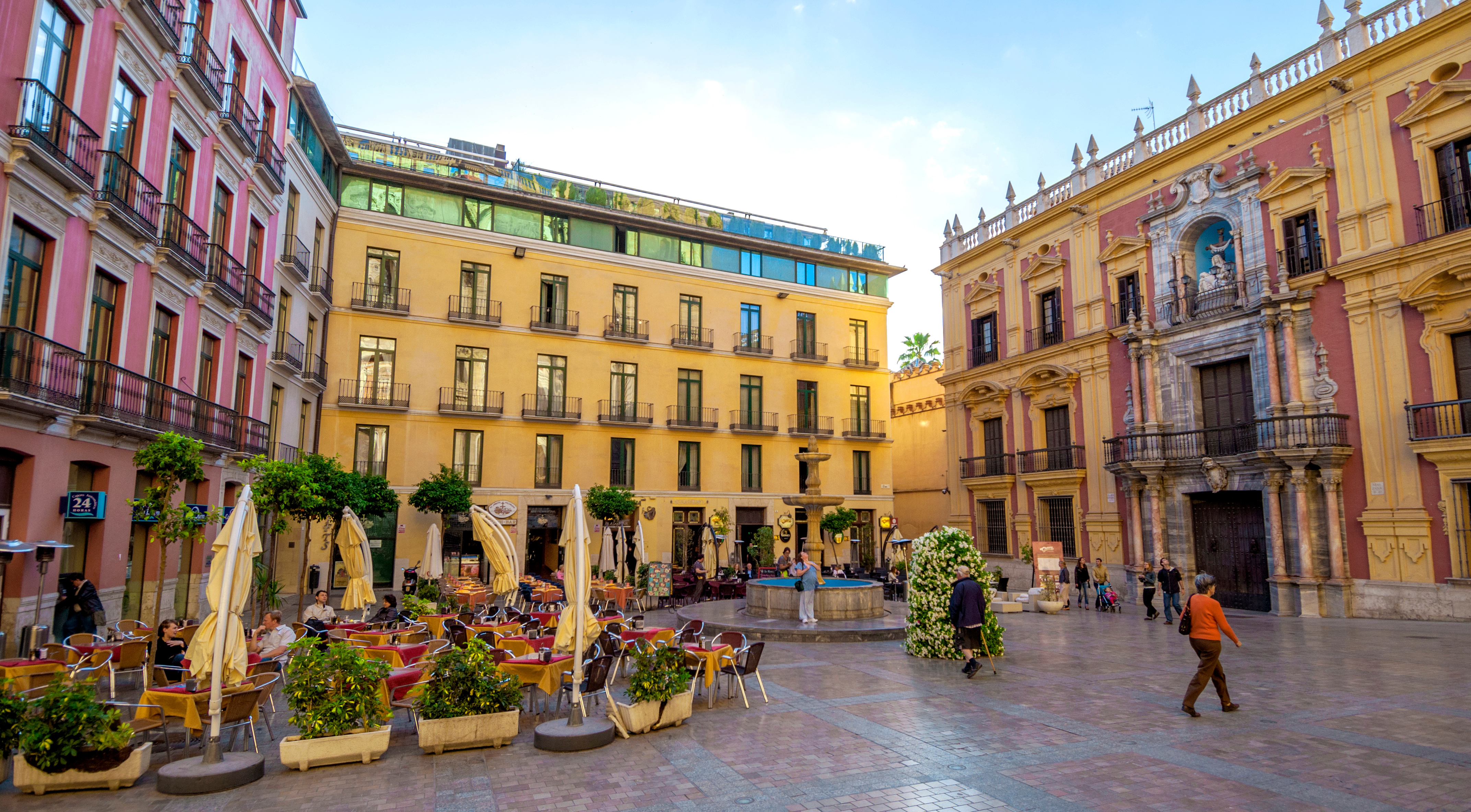 Hyggelig plads i Malaga med udendørs restaurantterrasser og smukke rosa og gule andalusiske bygninger