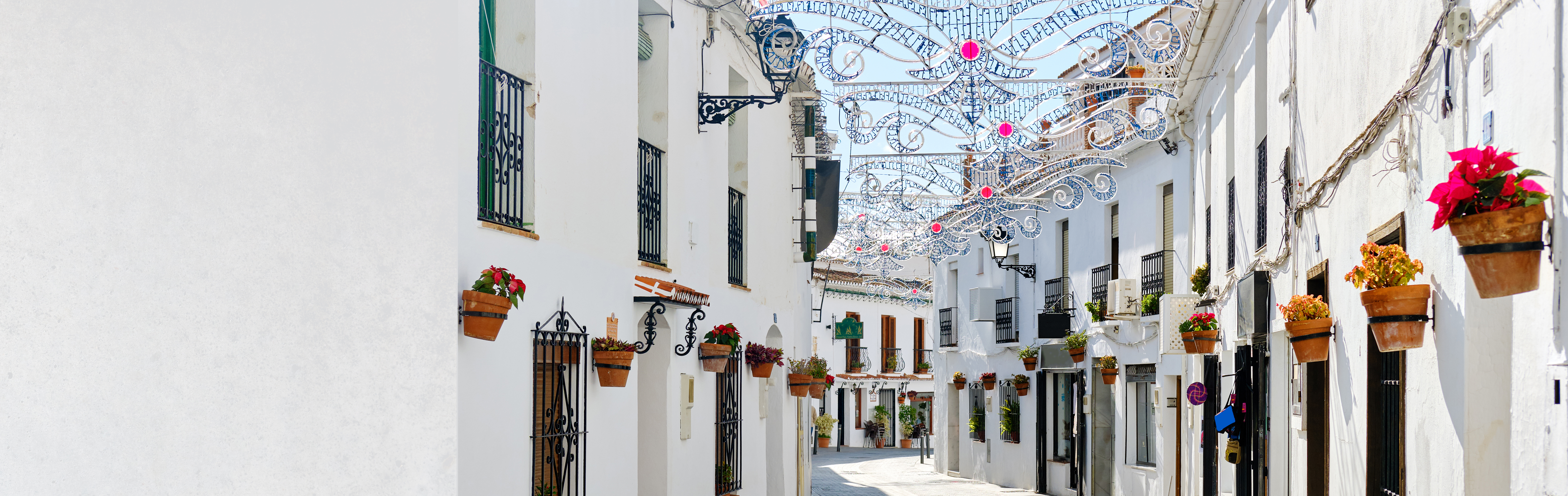 Traditionel andalusisk gade i Mijas med karakteristiske hvide bygninger, hængende blomsterkrukker og festlige dekorationer, perfekt feriedestination ved Costa del Sol