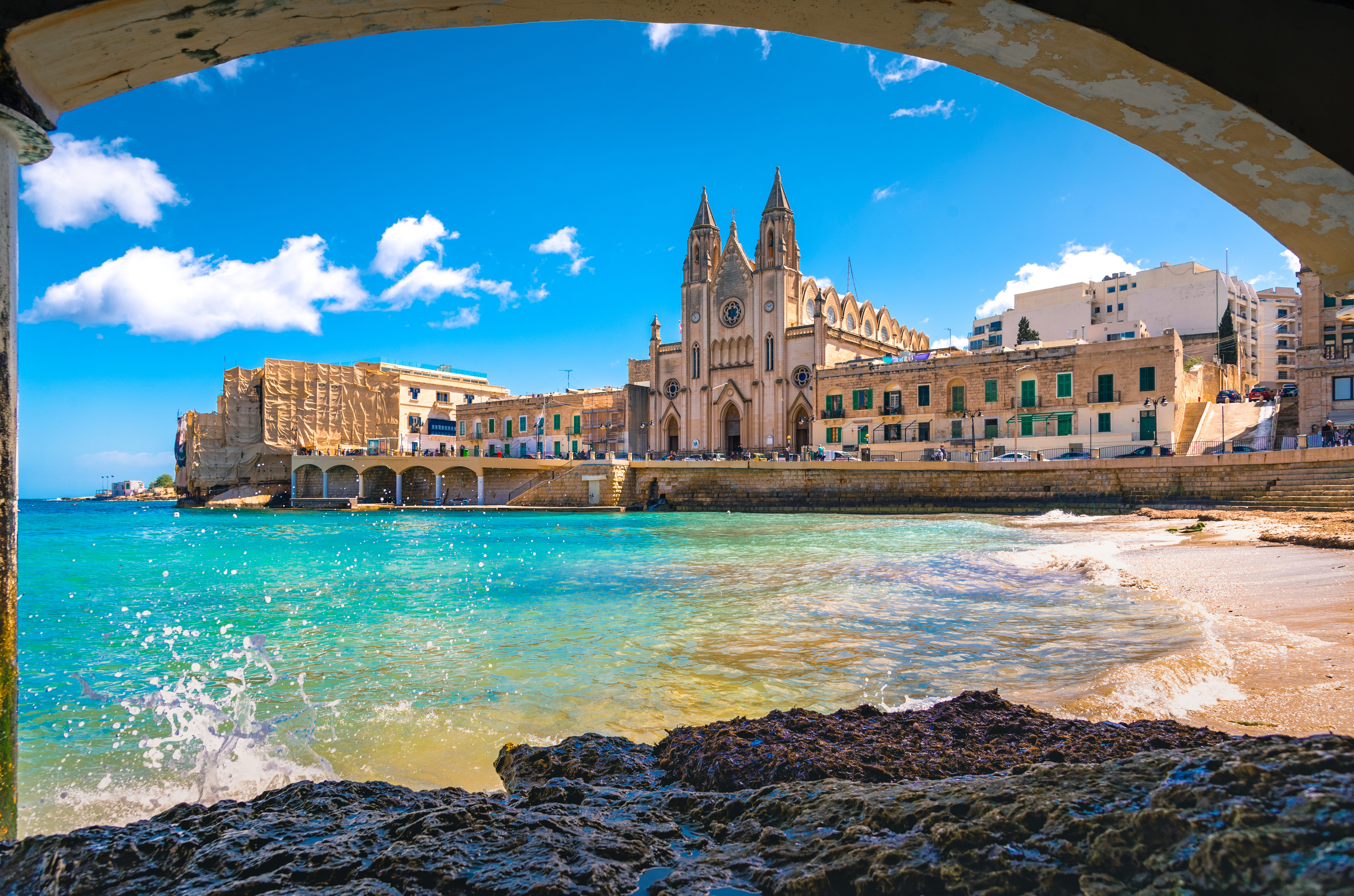 Idyllisk udsigt over St. Julian's på Malta med det smukke turkisblå Middelhav, gotisk kirke og traditionelle maltesiske bygninger ved Balluta Bay