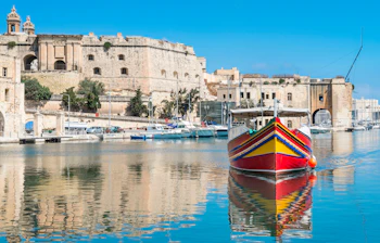 Farvestrålende luzzu fiskerbåd i Birgu havn Malta med kirketårne i baggrunden
