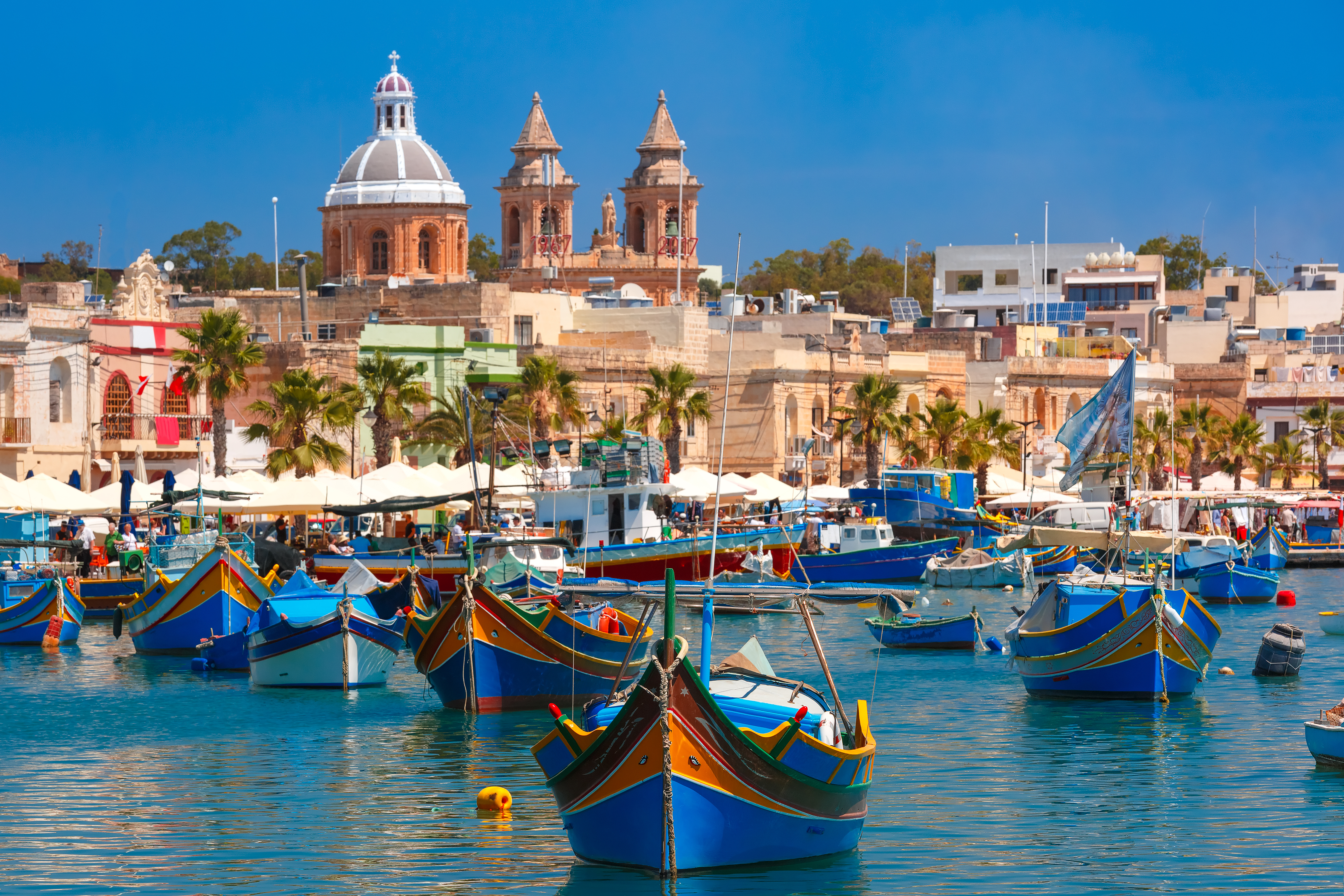 Malerisk udsigt over Marsaxlokk fiskehavn på Malta med traditionelle både og kirketårne